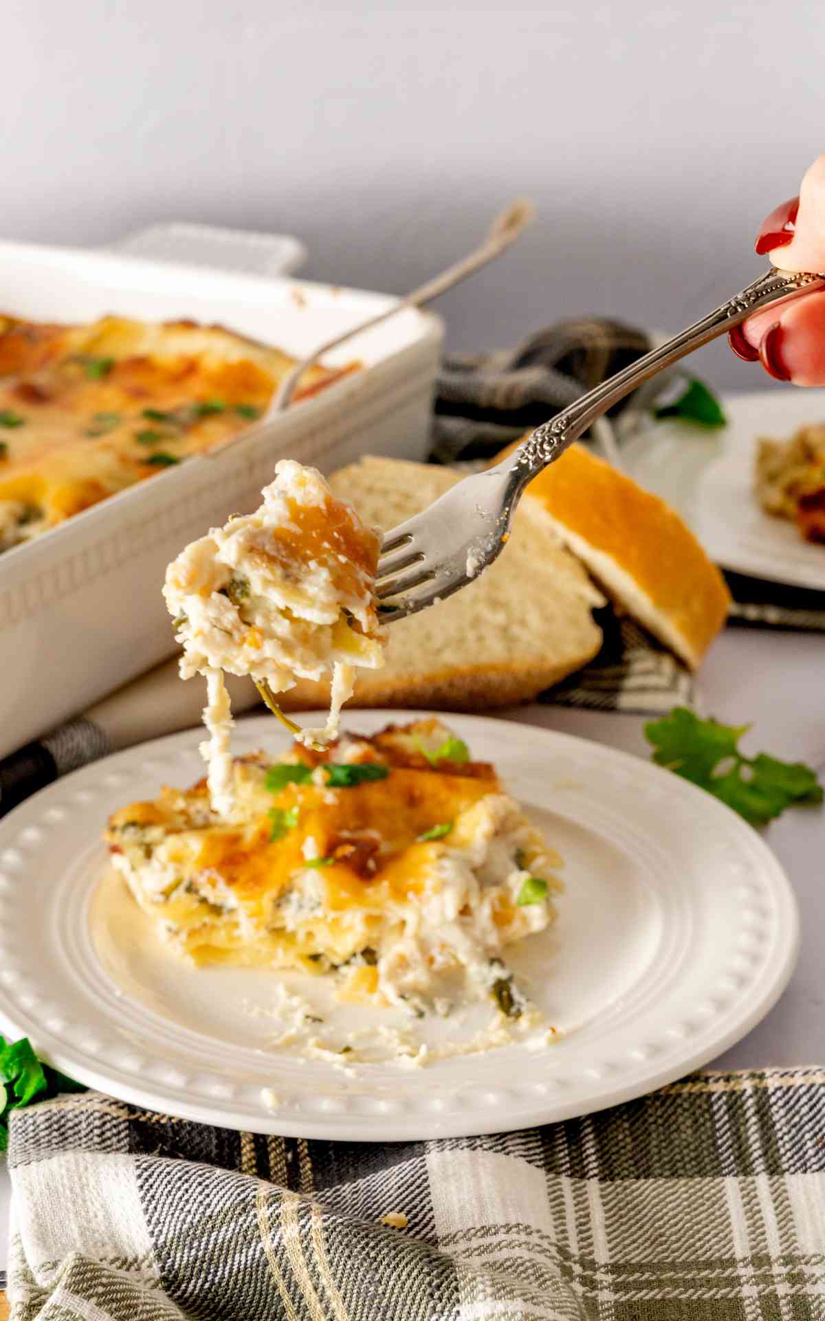 A fork holding up a bite of creamy chicken alfredo lasagna.