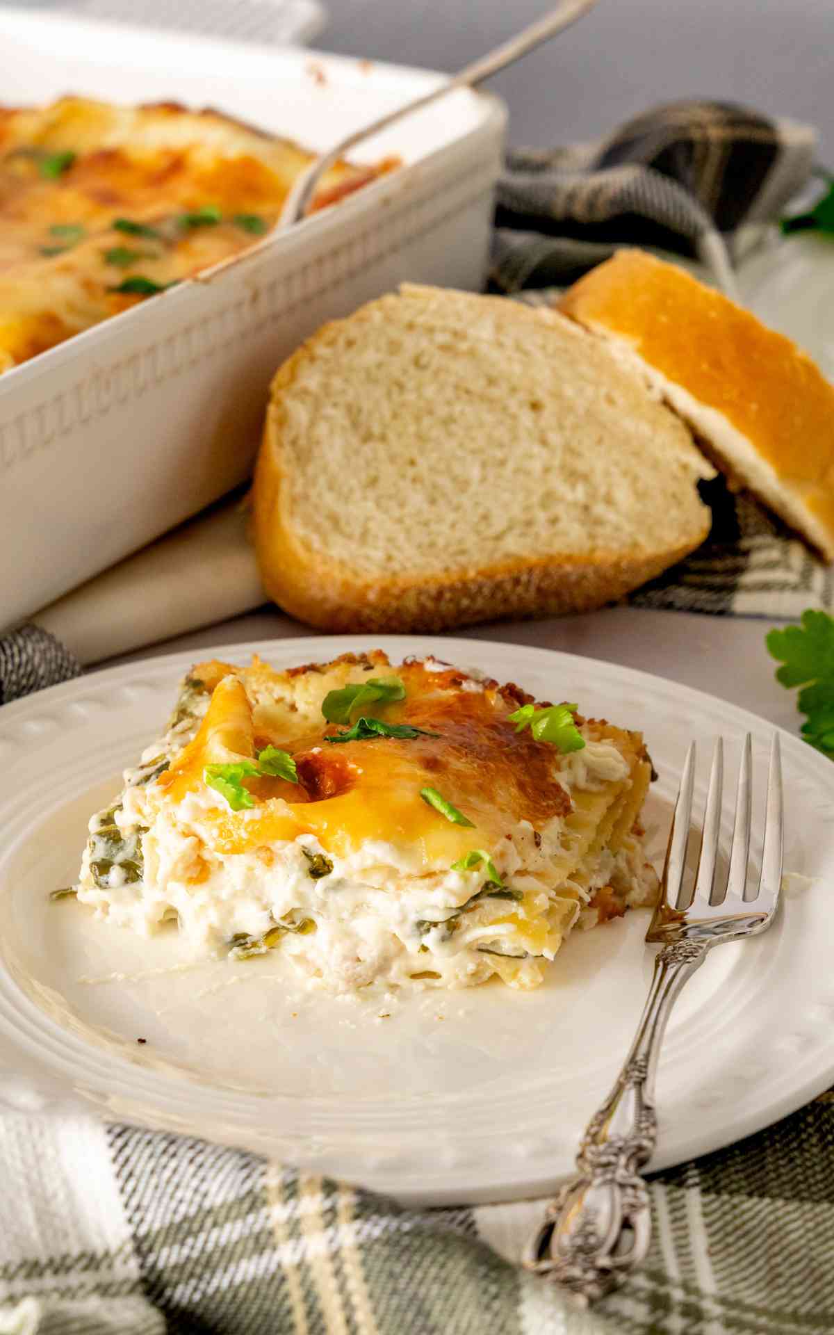 A plate of creamy chicken alfredo lasagna with sliced italian bread behind it.