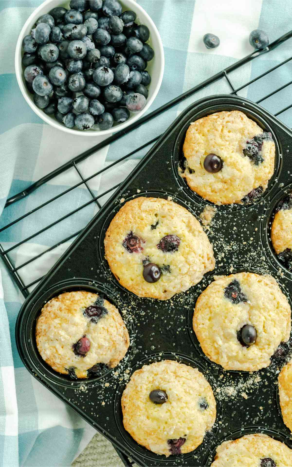 Cake mix blueberry muffins in a muffin pan with a bowl of blueberries.