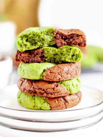 Matcha Cookies stacked on a plate with a cookie cut in half on top.