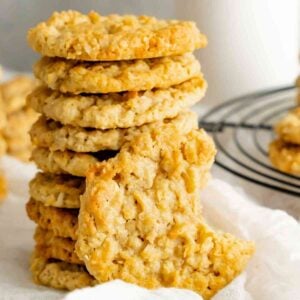 Stacked old fashioned cracker jack cookies on white linen with a classic milk jug.
