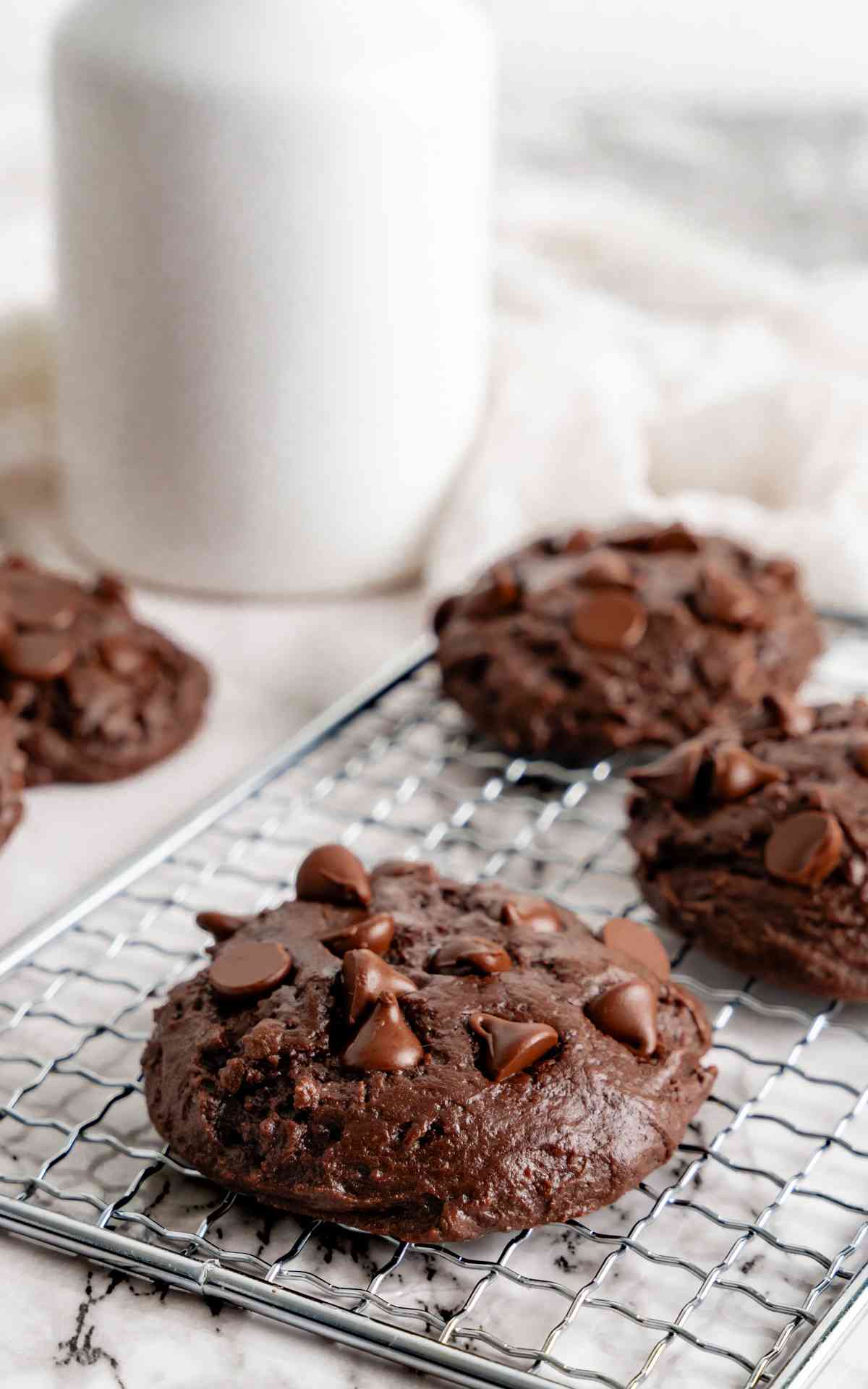 Three thick double chocolate fudge cookies on a cooling rack.