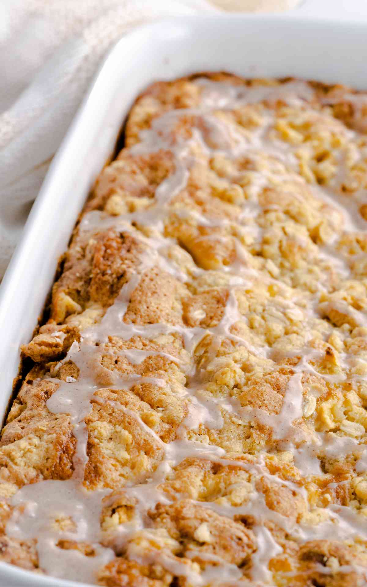 Apple Crumb Cake unsliced in a baking dish and iced.