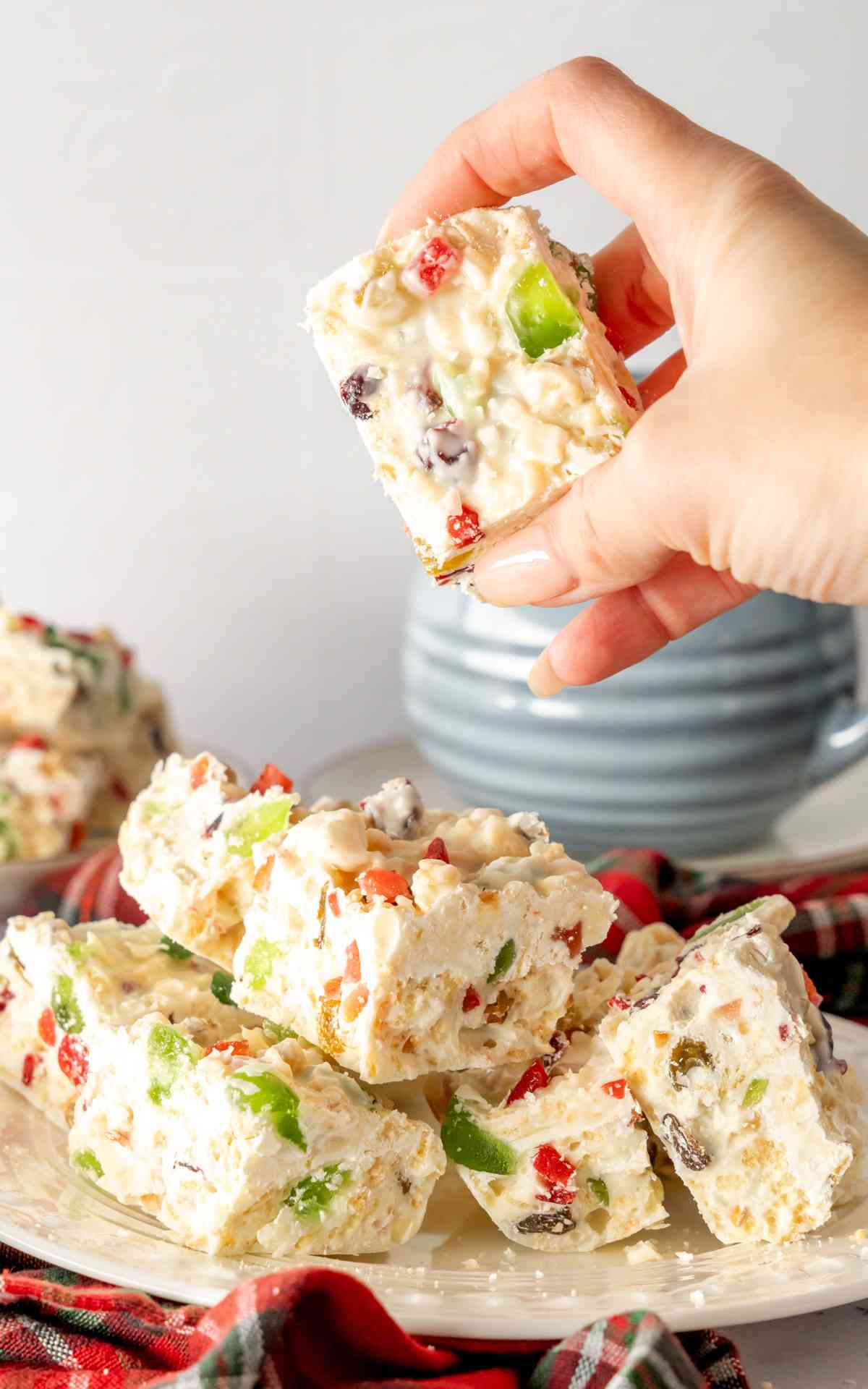 A manicured hand holding up White Christmas slice with a stack in the background.