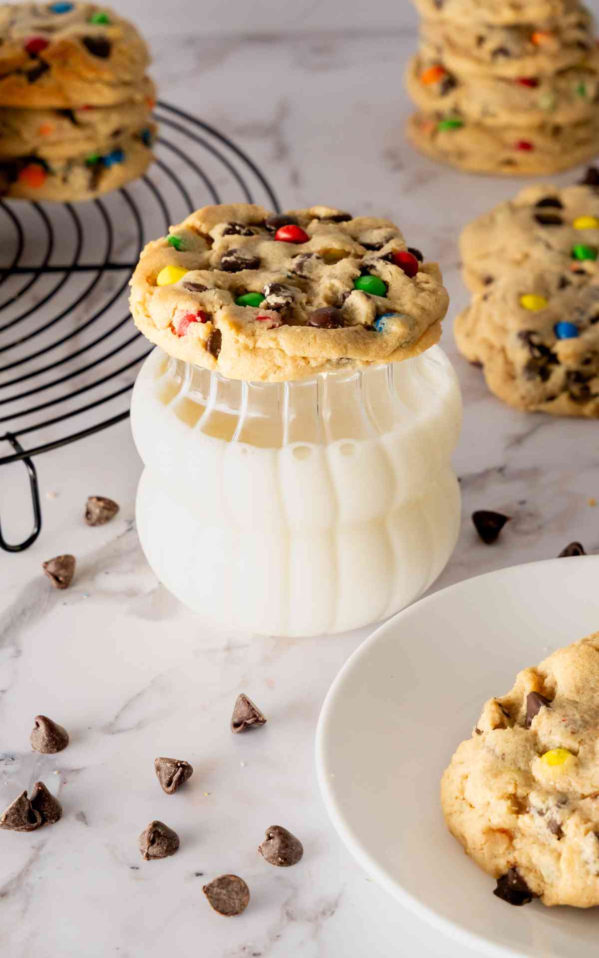 A peanut butter cookie with M&Ms and chocolate chips on a glass of milk.