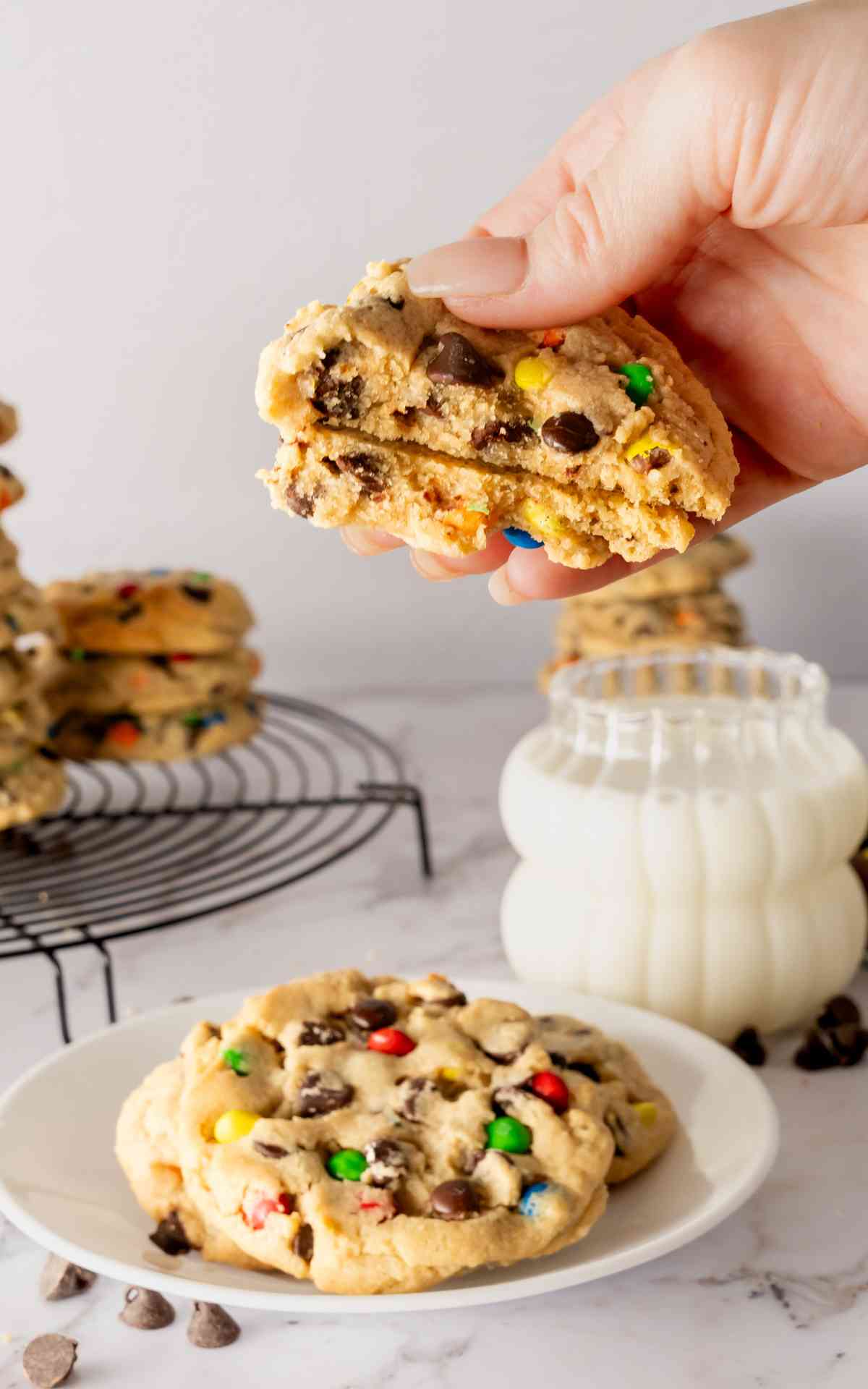 A thick M&M Peanut Butter Chocolate Chip Cookie broken in half and held in a hand.