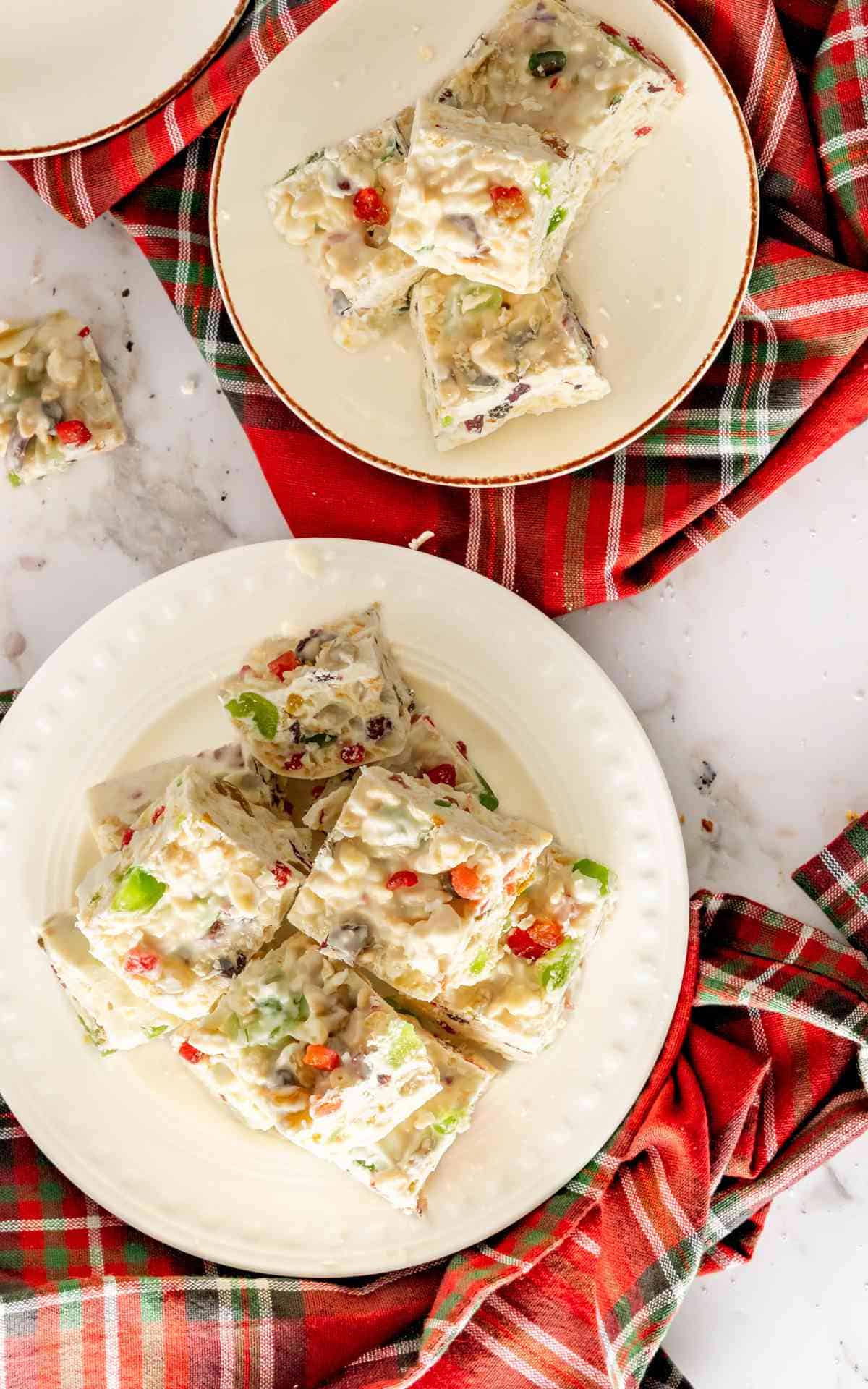 Birds eye view of two plates of White Christmas candy slices with red and green candied cherries and Rice Kripsies.