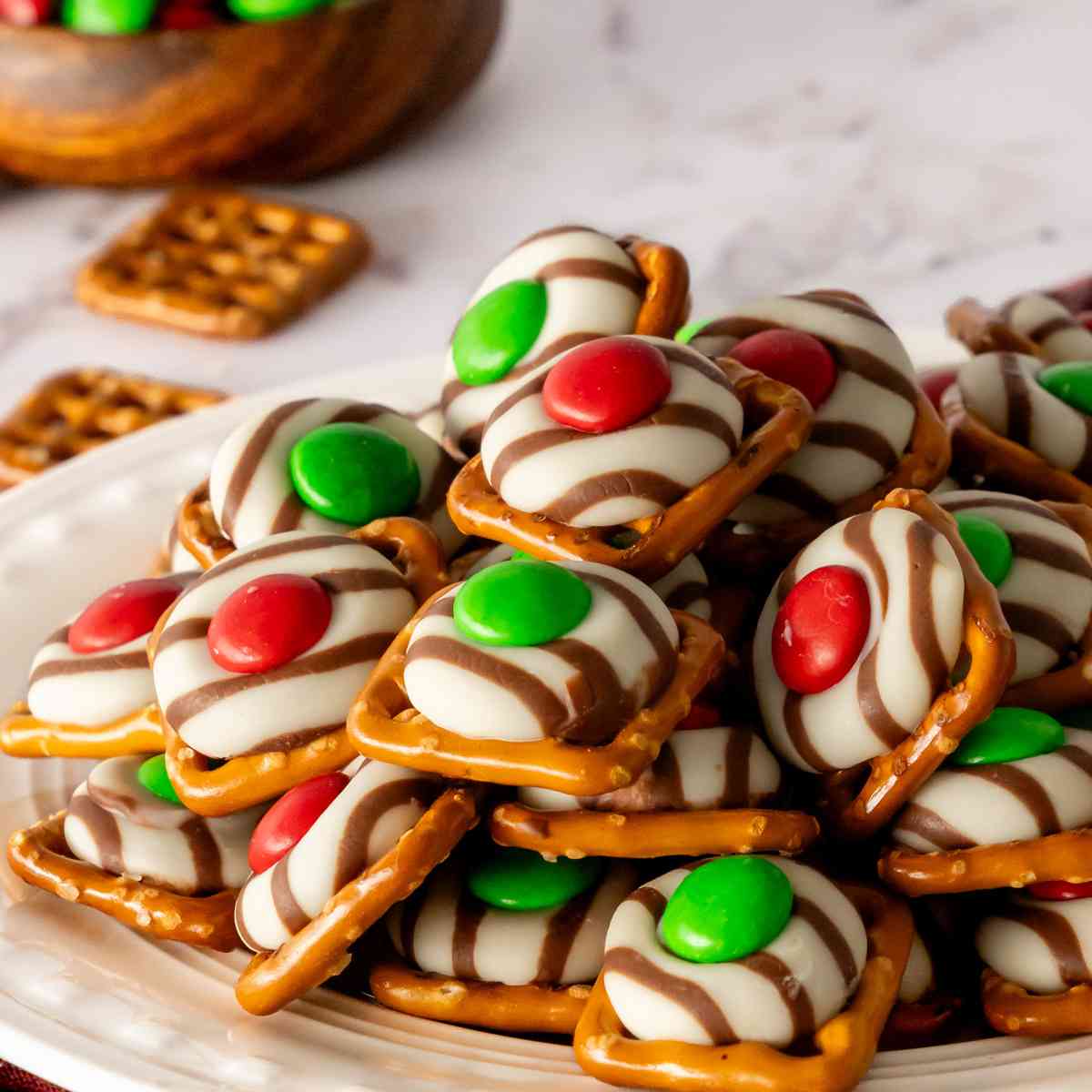 A plate of M&M Pretzels in Christmas colors on a white decorative plate.