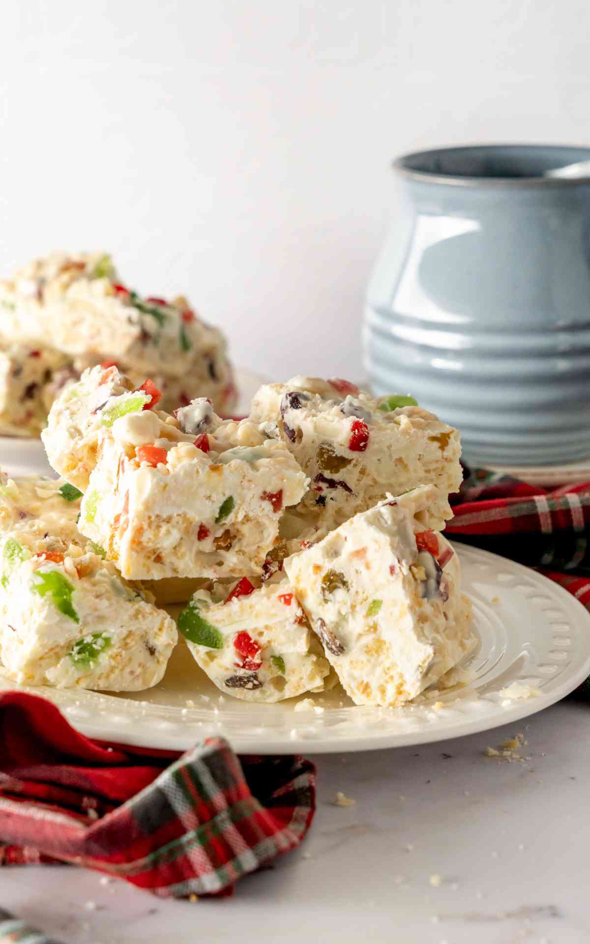 White Christmas slices stacked on a white decorative plate with red and green fruit.