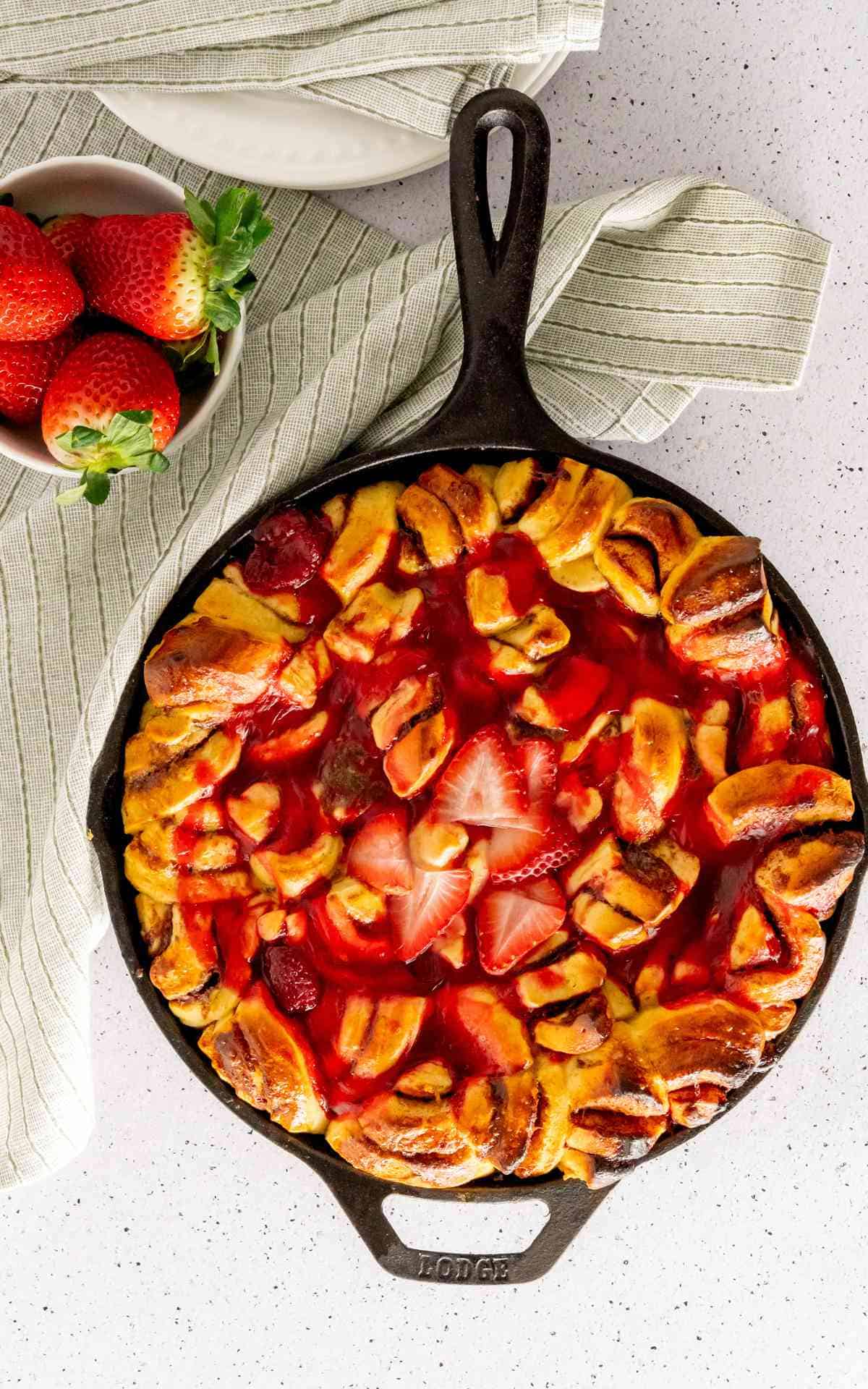 Overhead picture of a cinnamon roll bake with strawberry filling and fresh strawberries.
