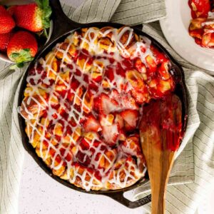 A serving utensil in a cast iron skillet of strawberry rolls made with strawberry filling.