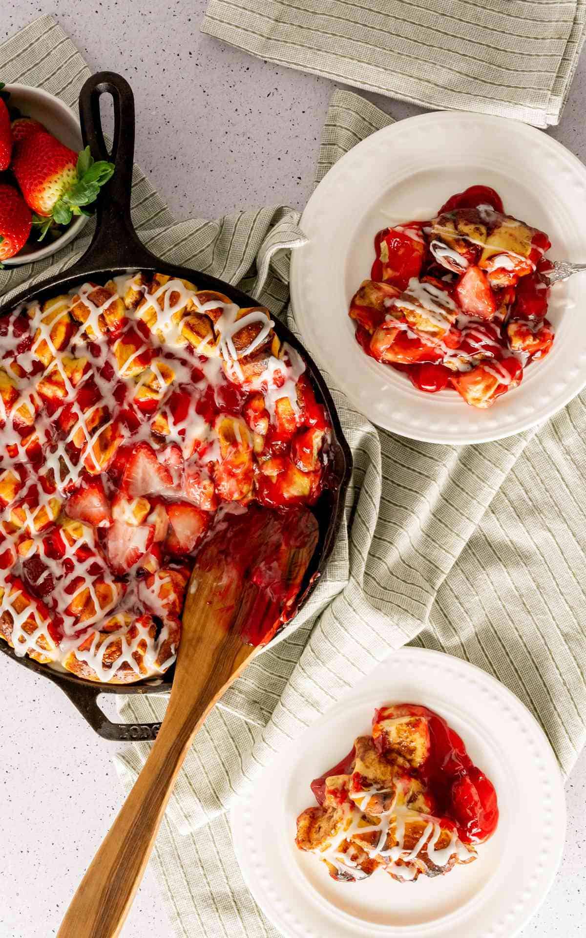 Two servings of cinnamon roll casserole with strawberries scooped out onto plates.
