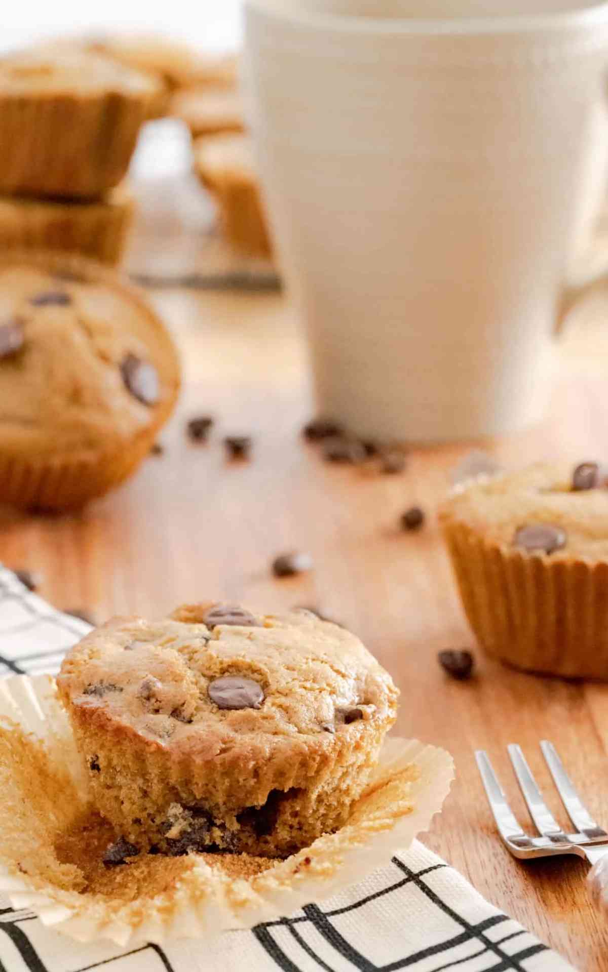 A cup of coffee behind a cappuccino muffin with the liner peeled away.