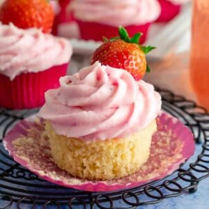 A strawberry lemonade cupcake with a fresh strawberry pressed into the frosting.