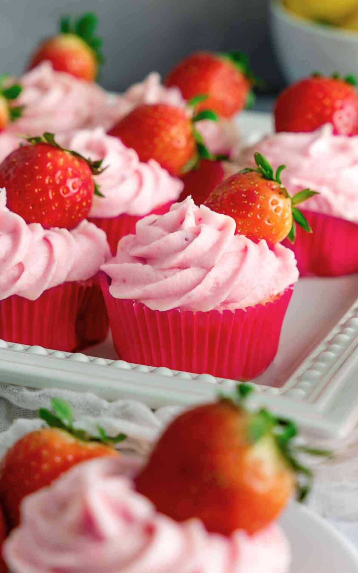 Strawberry lemonade cupcakes in pink liners on a decorative plate.