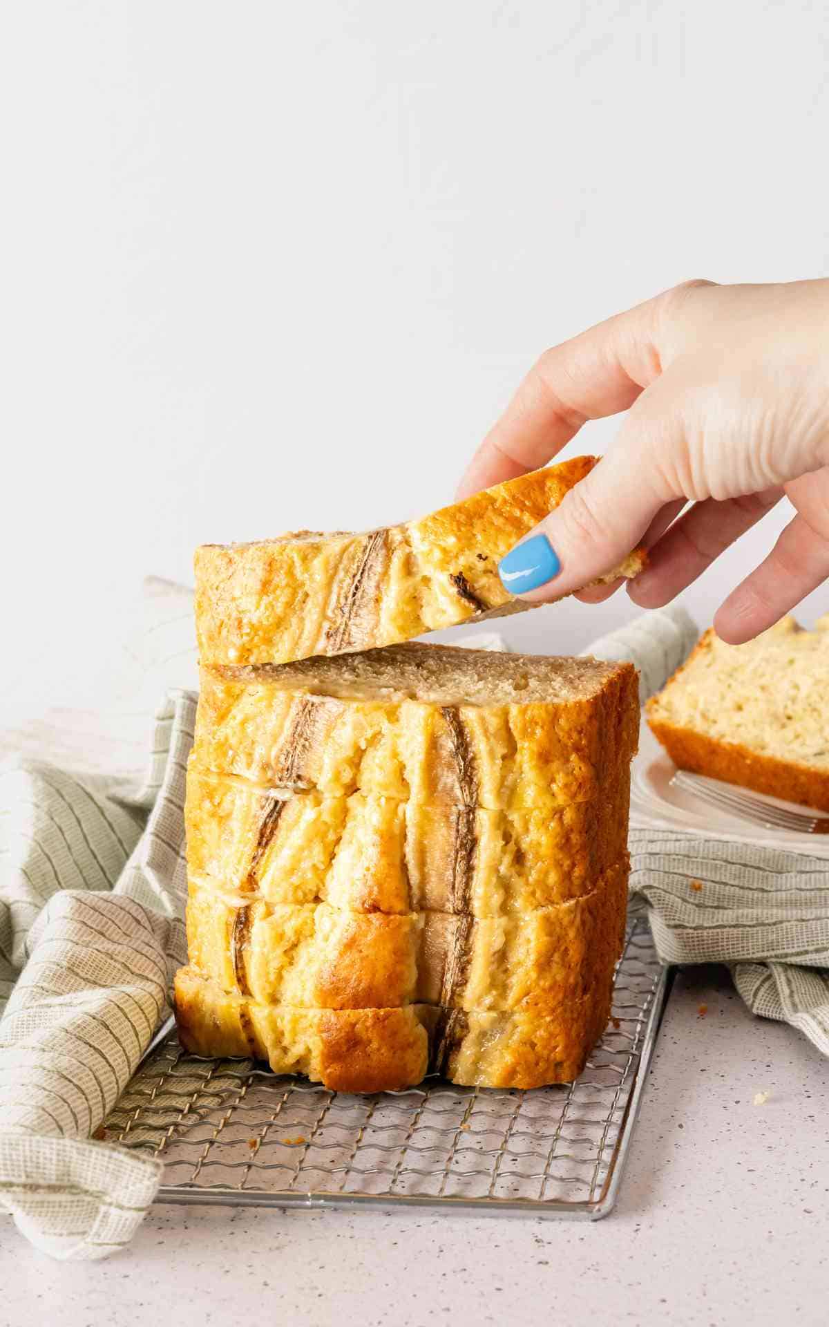 A hand picking up a banana loaf slice from a stack.
