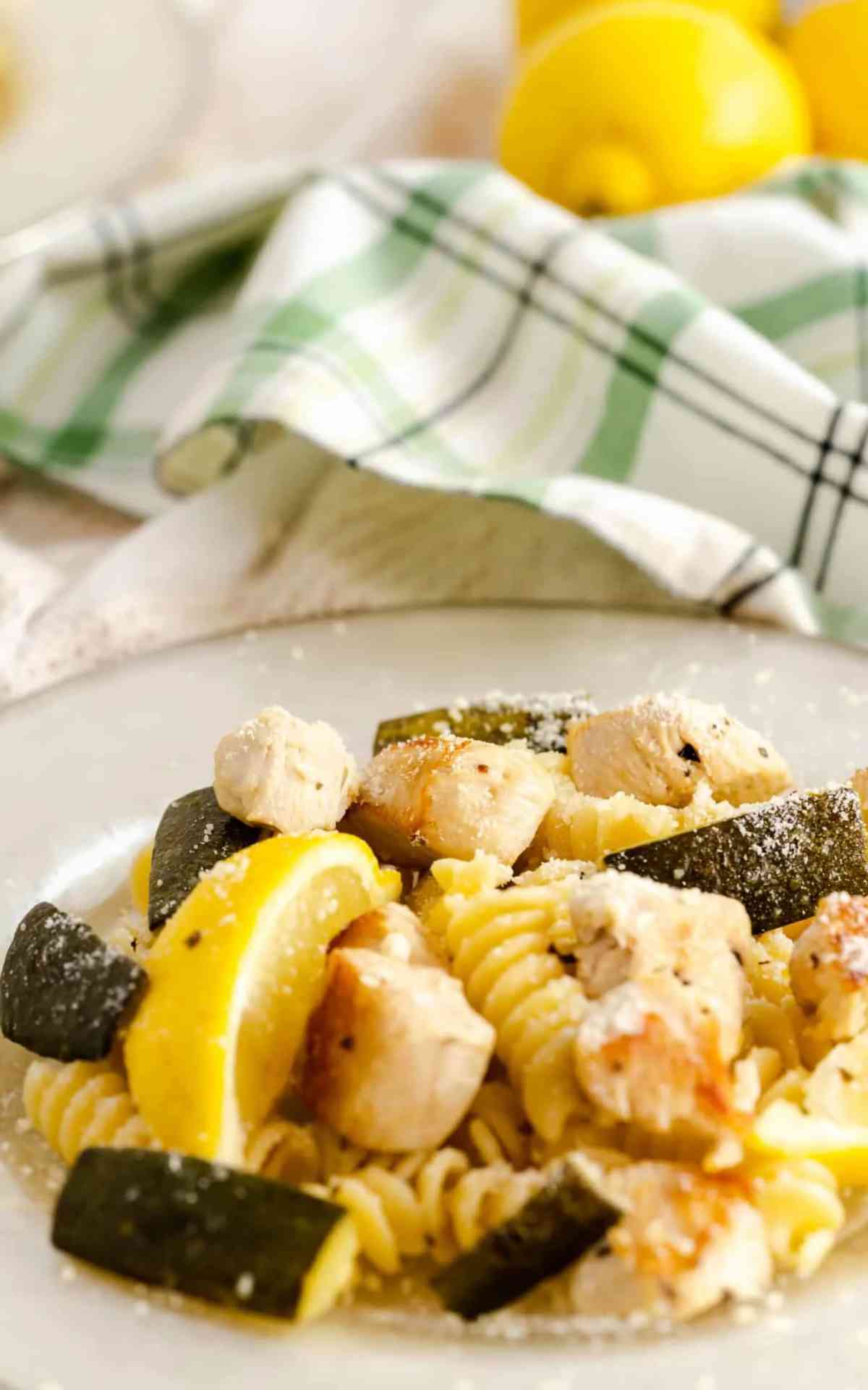 A plate of chicken zucchini pasta and lemon slices.