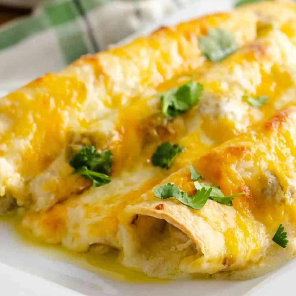 A serving of white chicken enchiladas topped with cilantro on a white plate.