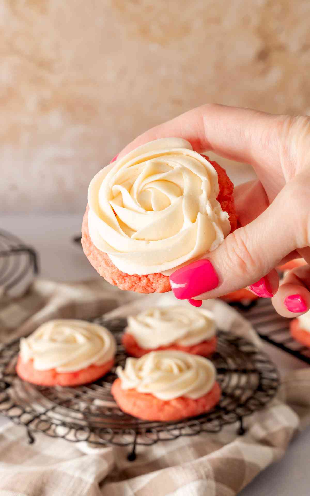 A manicured hand holding up a frosted pink lemonade cookie.