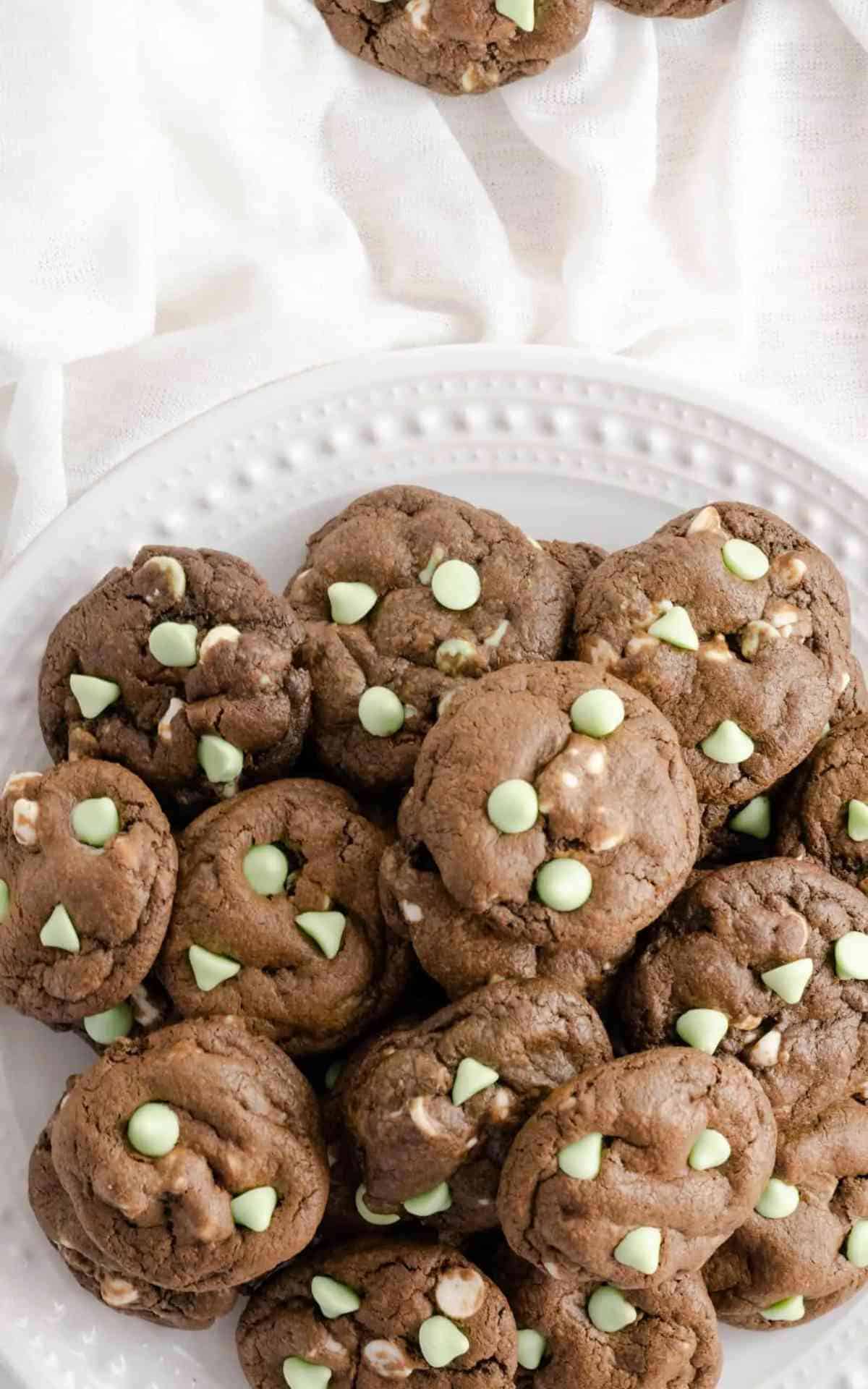 Mint chocolate cookies stacked on a a white decorative serving platter.