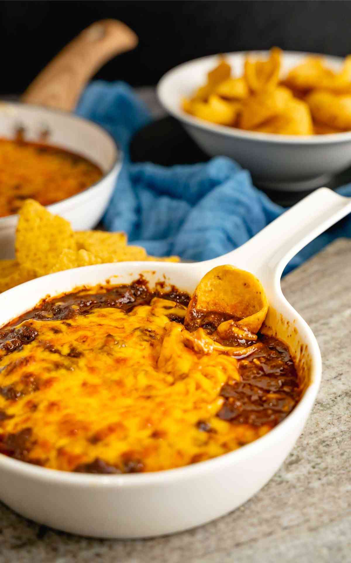 A white dish with handle with hot skyline chili dip and frito scoop.