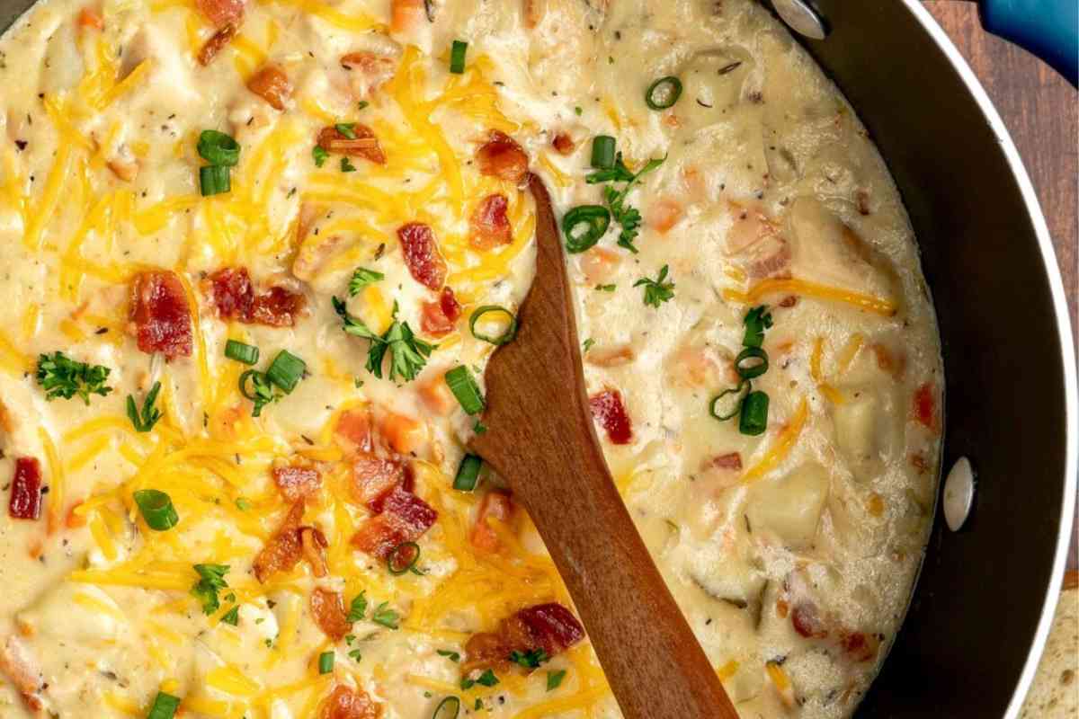 Pan with chicken and potato soup with toppings and a wooden spoon.