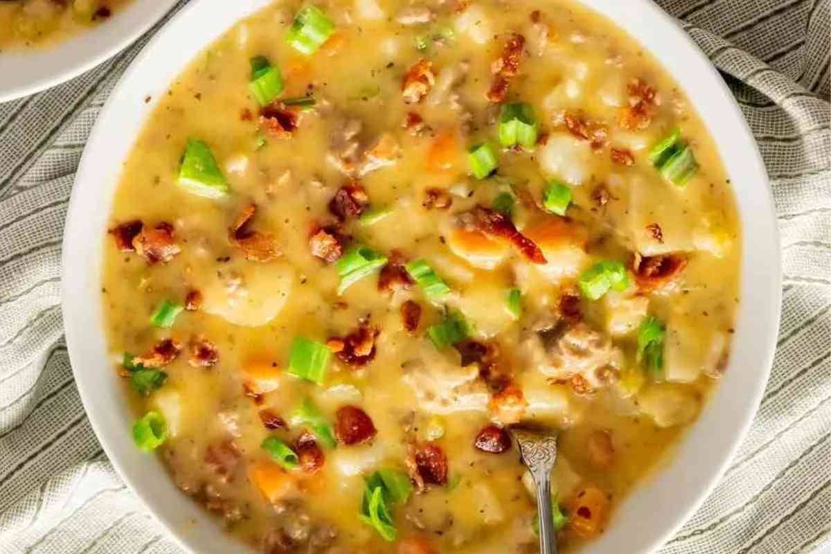 A bowl of cheeseburger soup with chopped bacon, scallions, and shredded cheese.