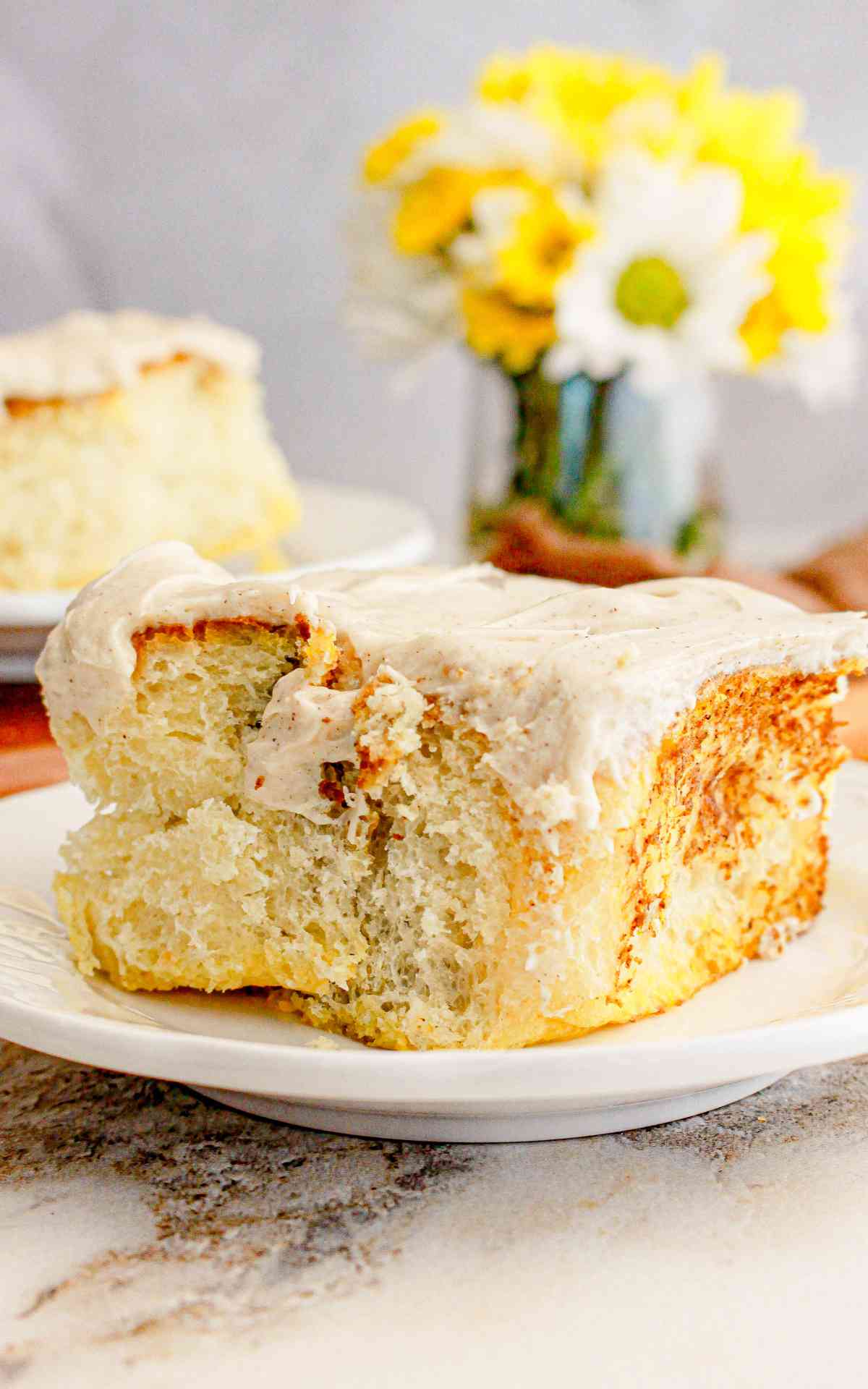 A freshly baked pumpkin spice cinnamon roll on a plate with flowers in the background.