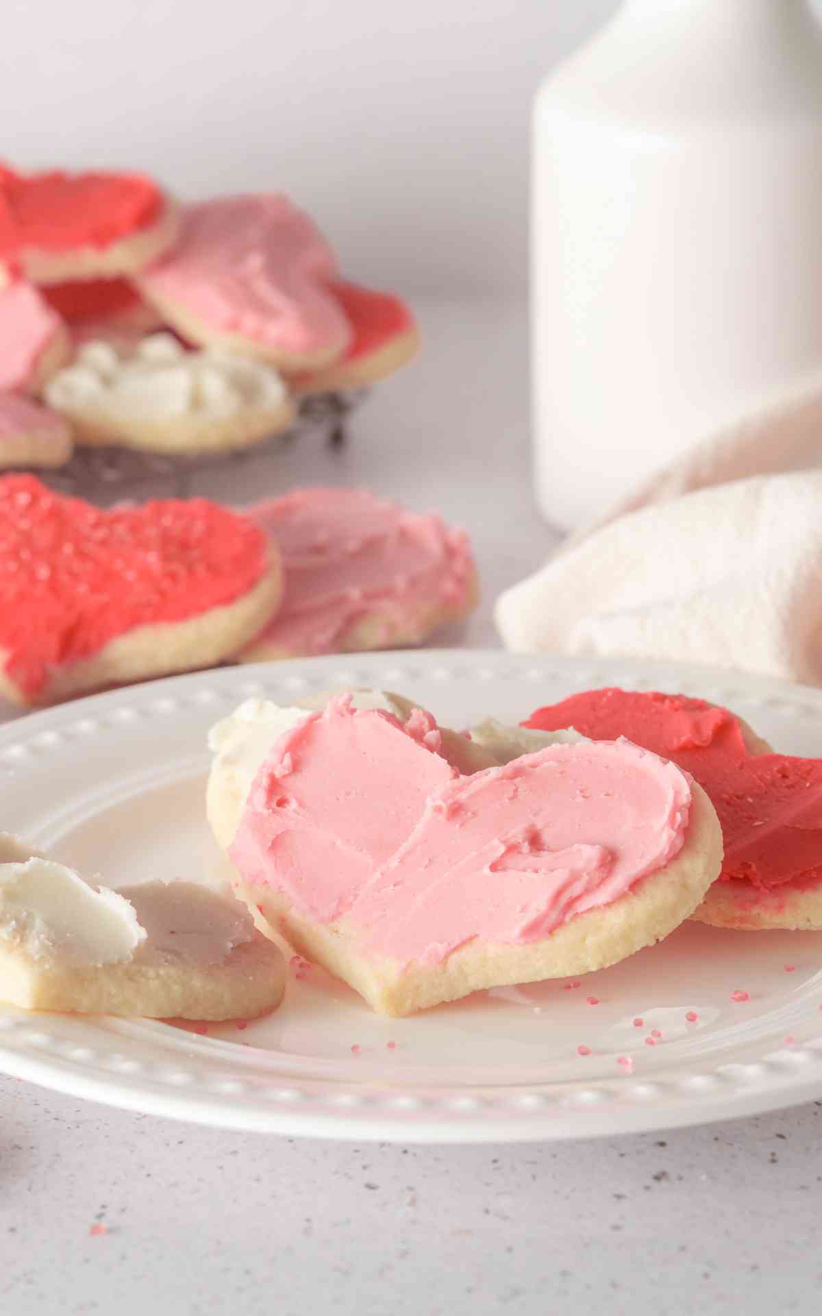 A white plate with heart shaped cream cheese sugar cookies with buttercream frosting.