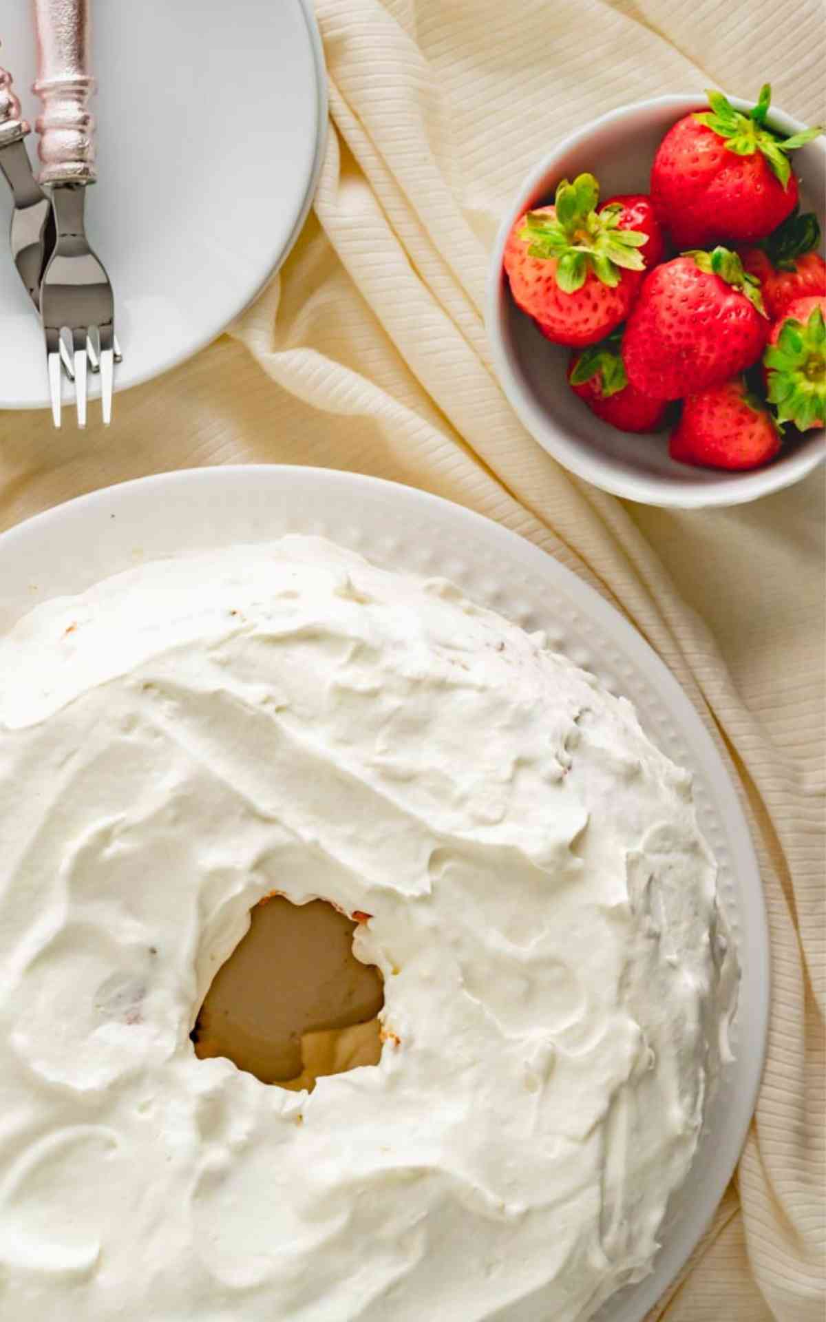 A whole angel food cake with a bowl of fresh strawberries.