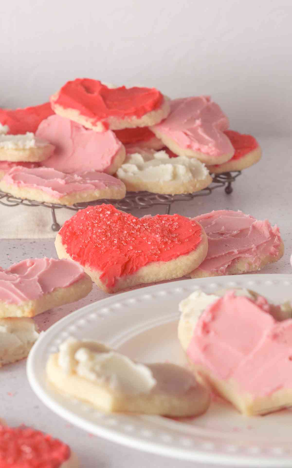 Red white and pink heart shaped cream cheese sugar cookies on a white plate and wire rack.
