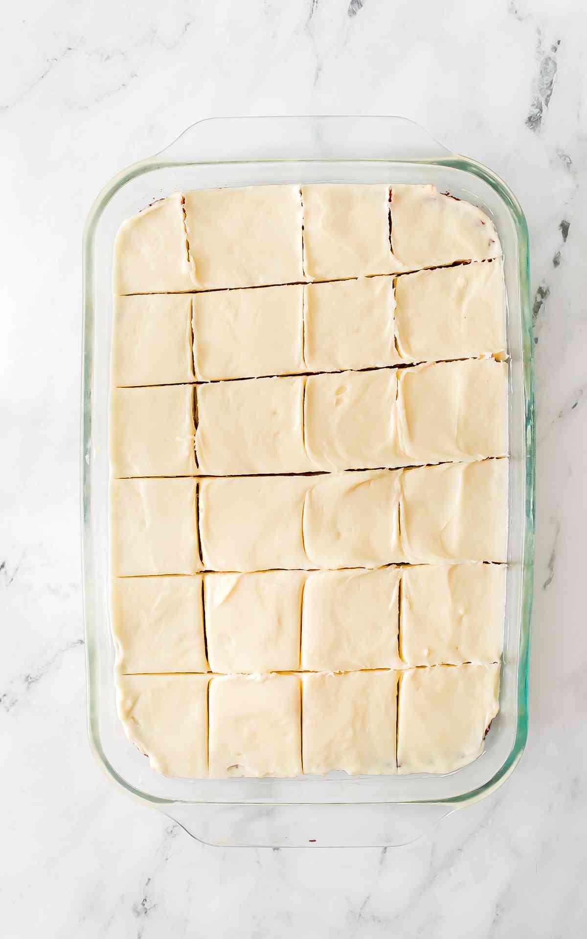 Sliced cream cheese frosted red velvet bars in a glass dish.