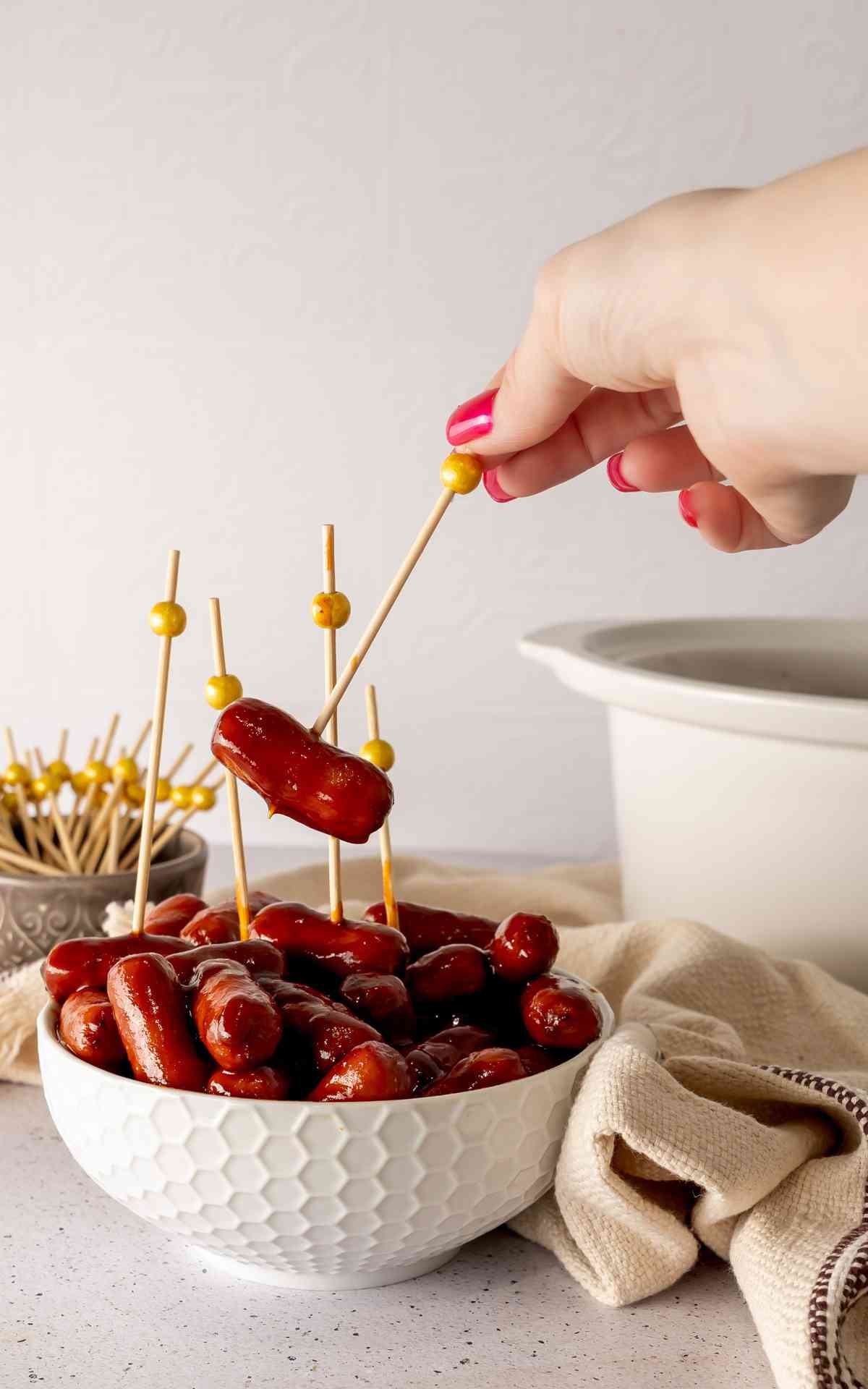 A hand picking up a cocktail pick stuck in a cocktail weenie.