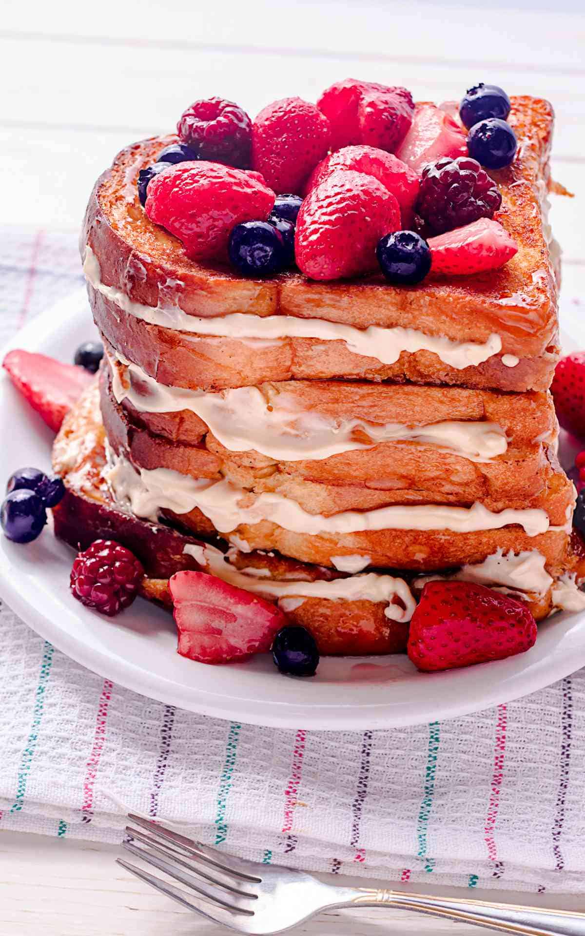 A plate of four stacked French toast sandwiches with berries.