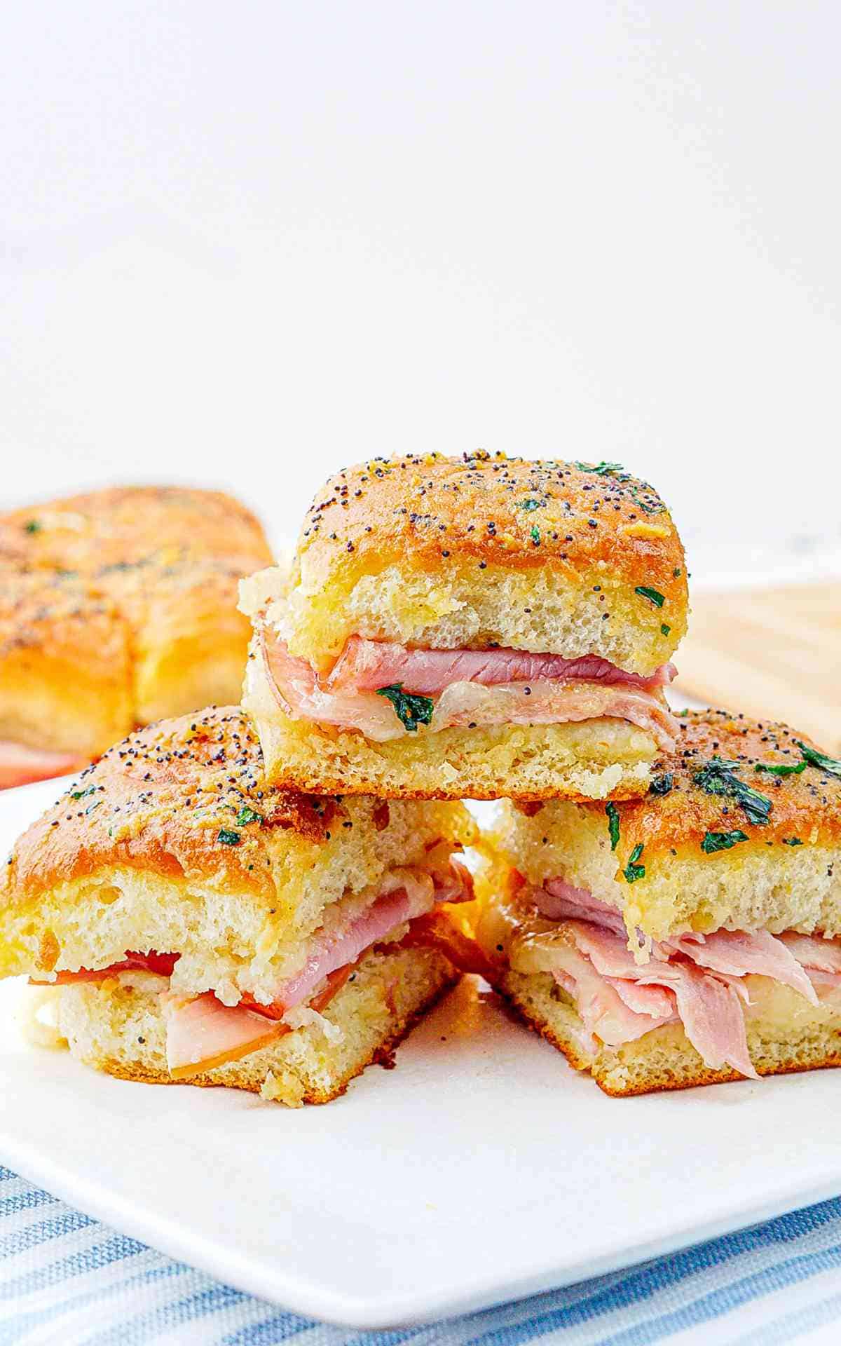A stack of ham and cheese sliders on a white plate.
