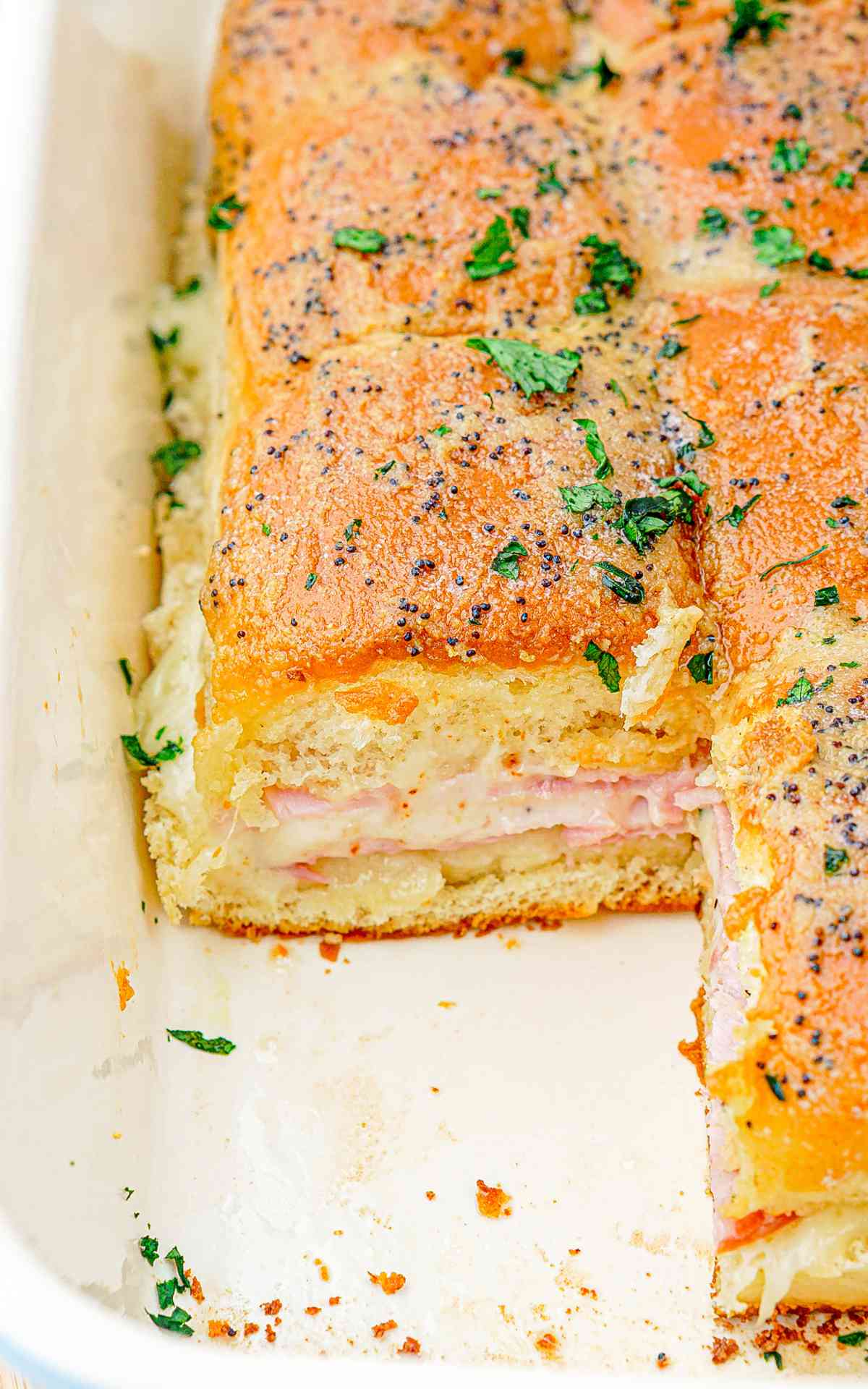 Side view of a ham and cheese slider in a baking dish.