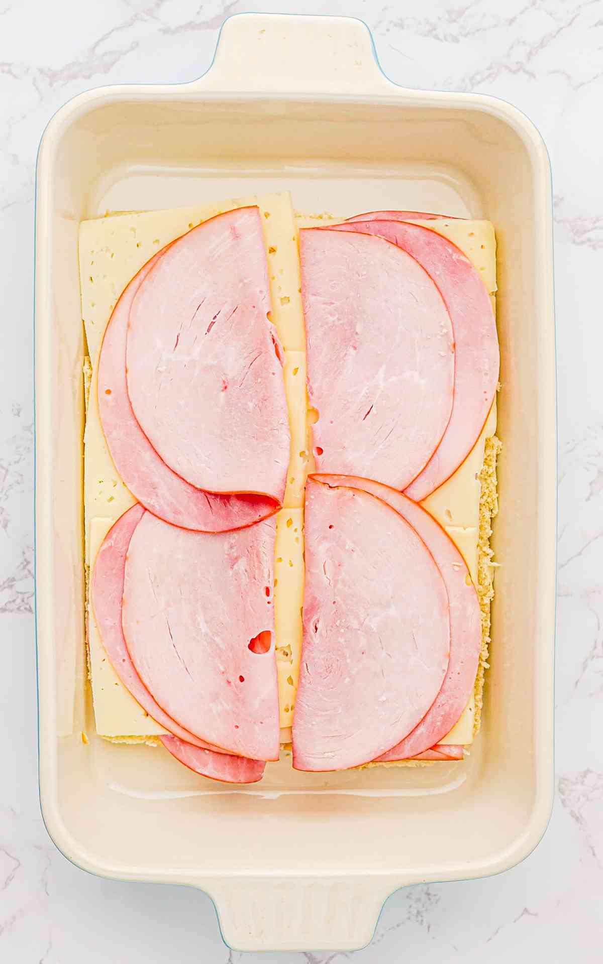 Swiss cheese and ham on the a layer of bottom rolls doe ham and cheese sliders.