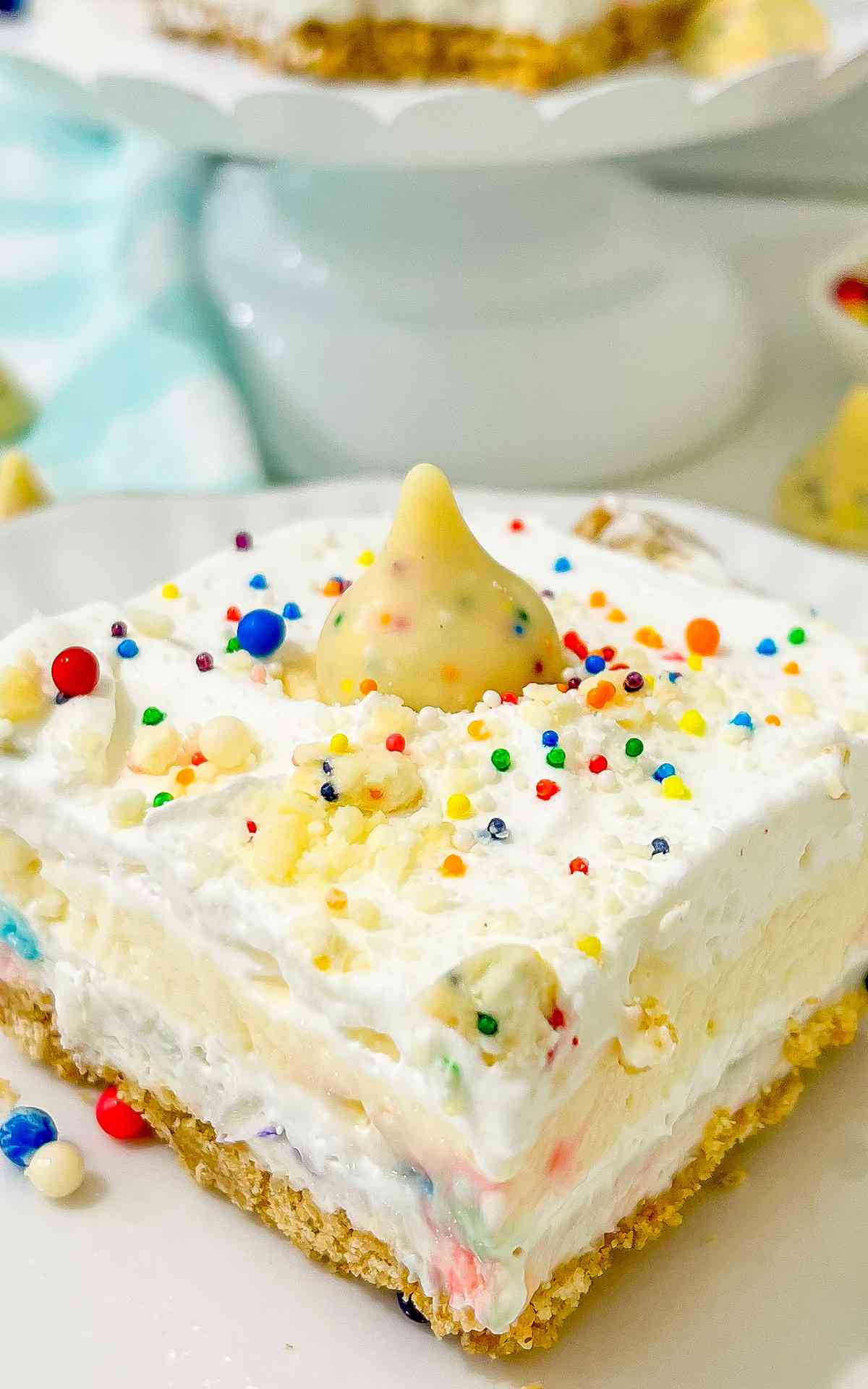 A square slice of birthday cheesecake topped with colorful sprinkles.