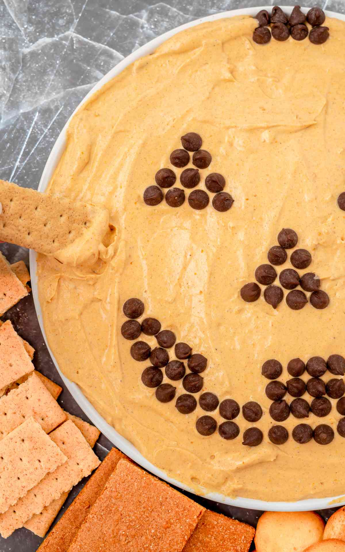 A graham cracker being dipped into pumpkin dip with a Jack o Lantern face.