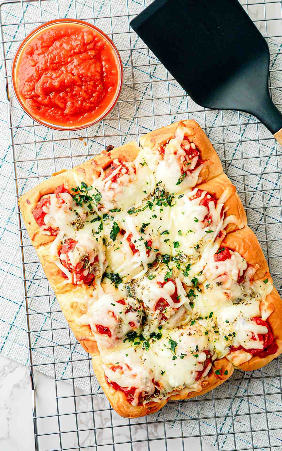 Baked meatball sliders on a wire rack with a bowl of marinara sauce for serving.