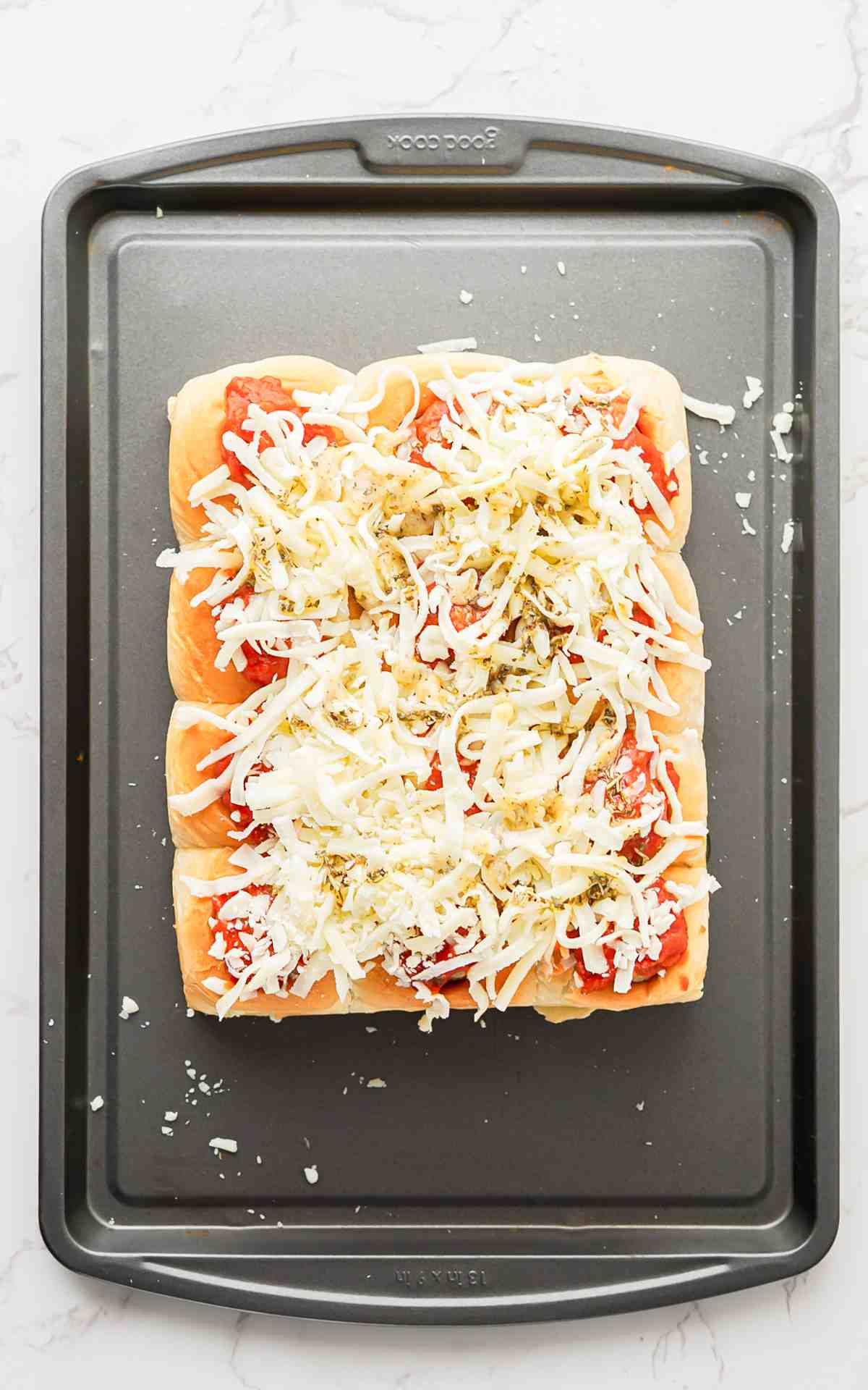 Cheese spread on top of hawaiian roll meatball sliders before being baked.