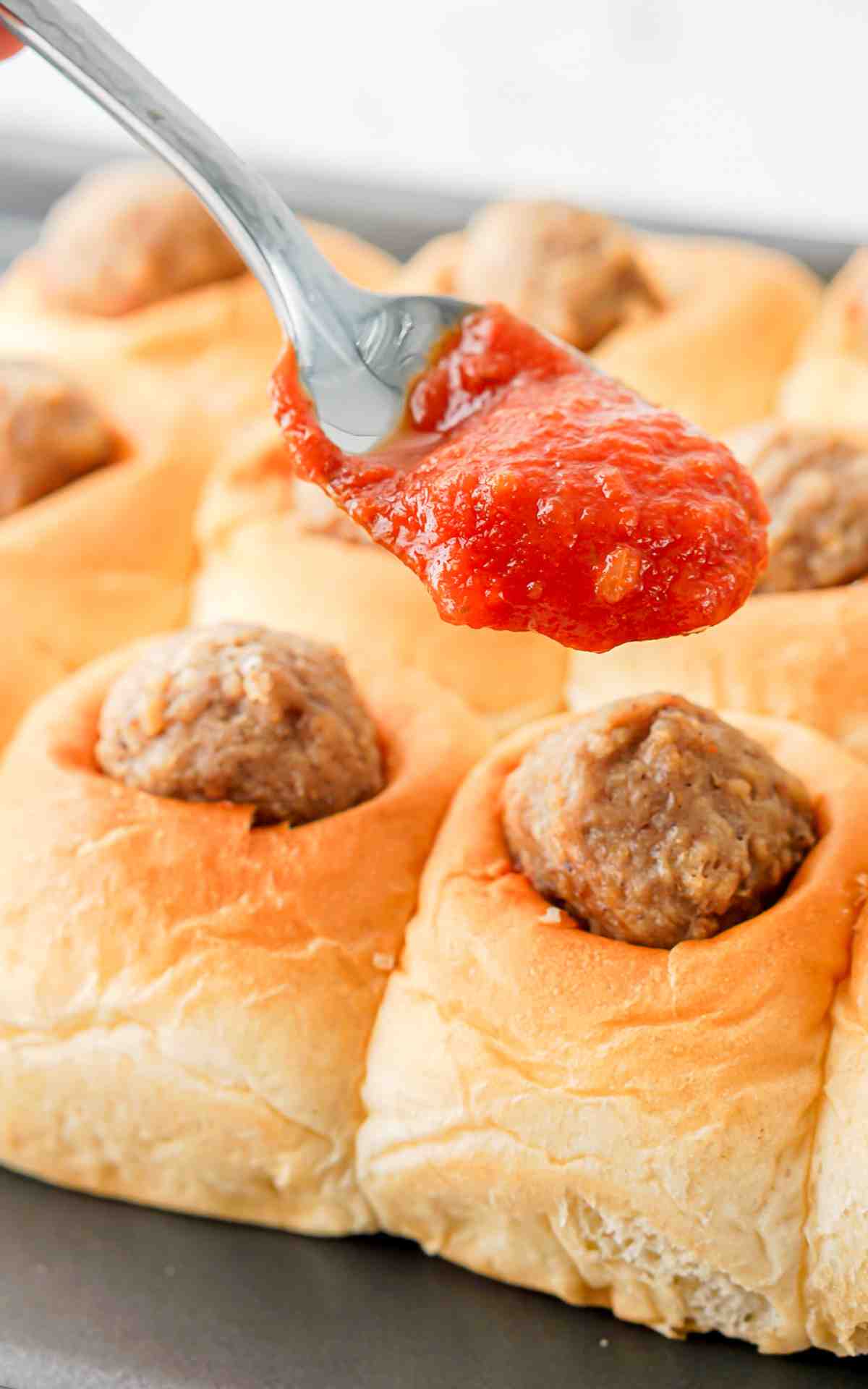 Marinara being spooned on top of the meatballs.