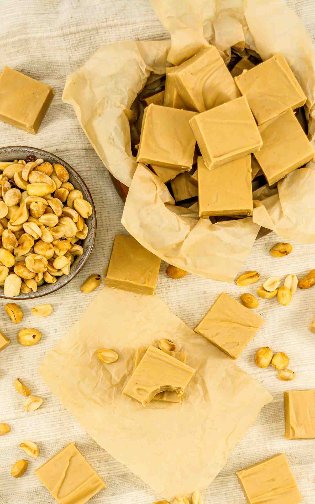 A tin of 2 ingredient peanut butter fudge with peanuts and fudge scattered on counter.