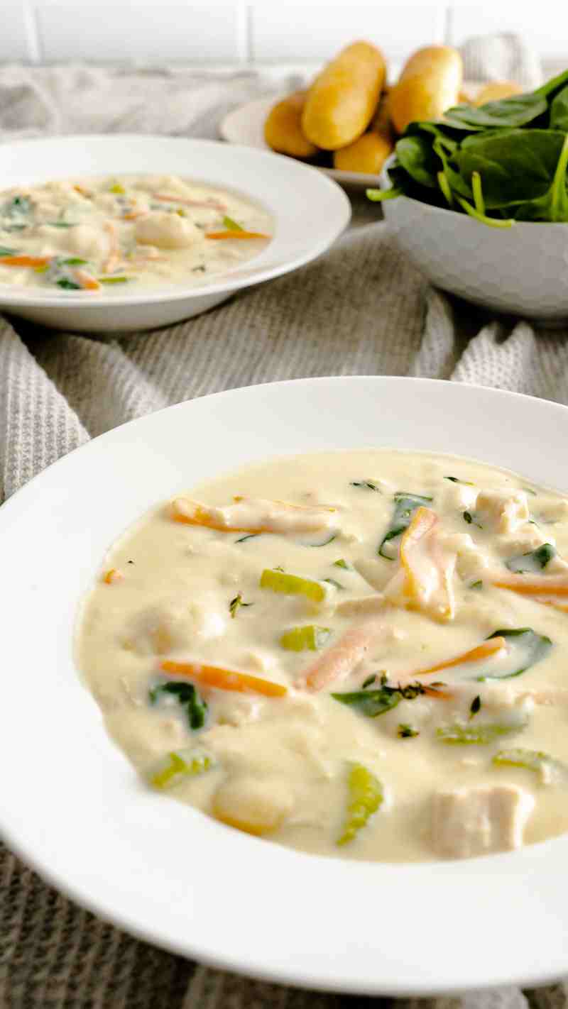 Two bowls of chicken gnocchi soup with breadsticks and spinach.