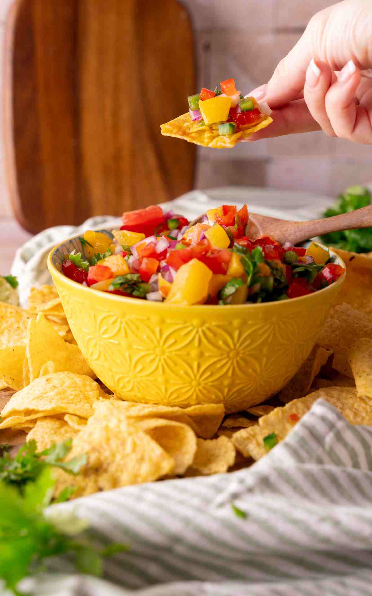 A hand holding up a chip with peach salsa on it.