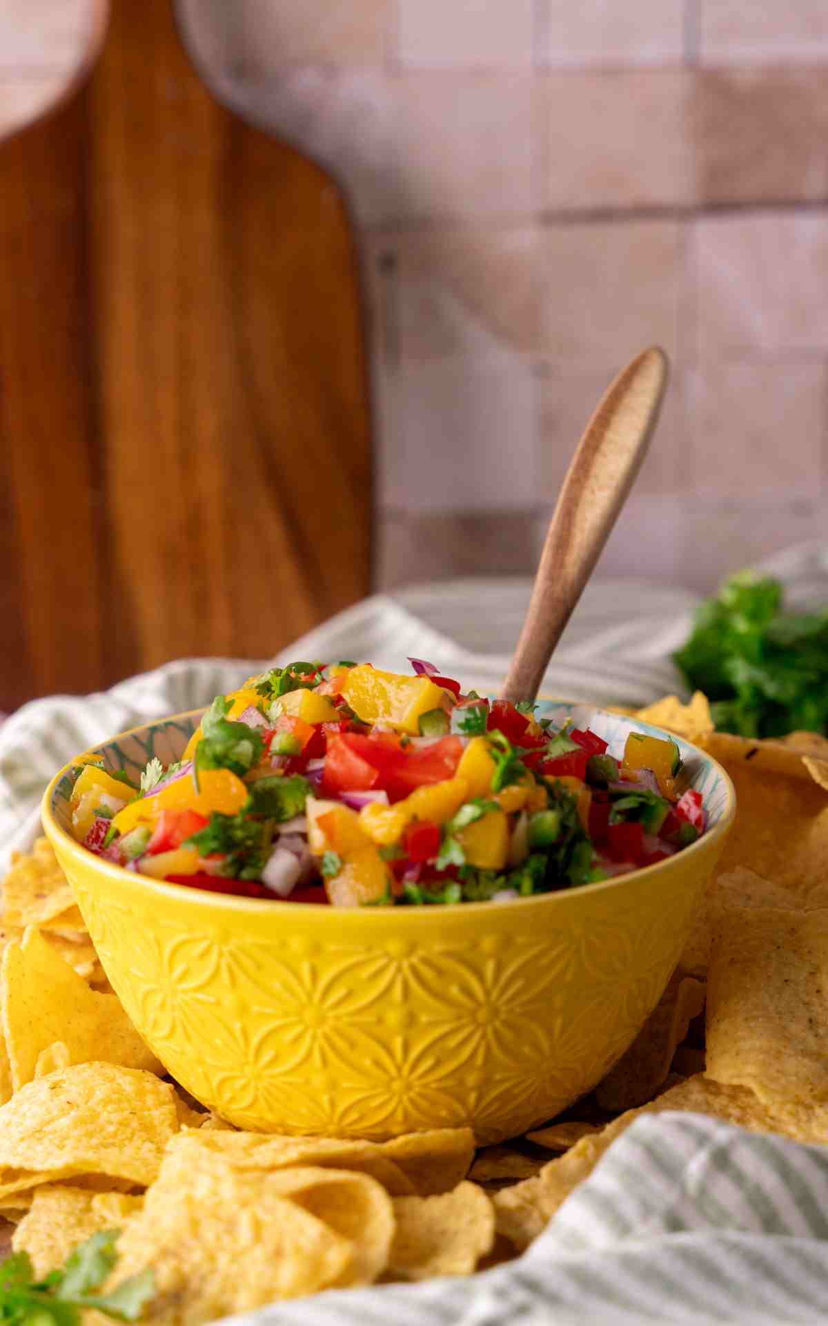 A wooden spoon in a yellow bowl of fresh peach salsa for serving.