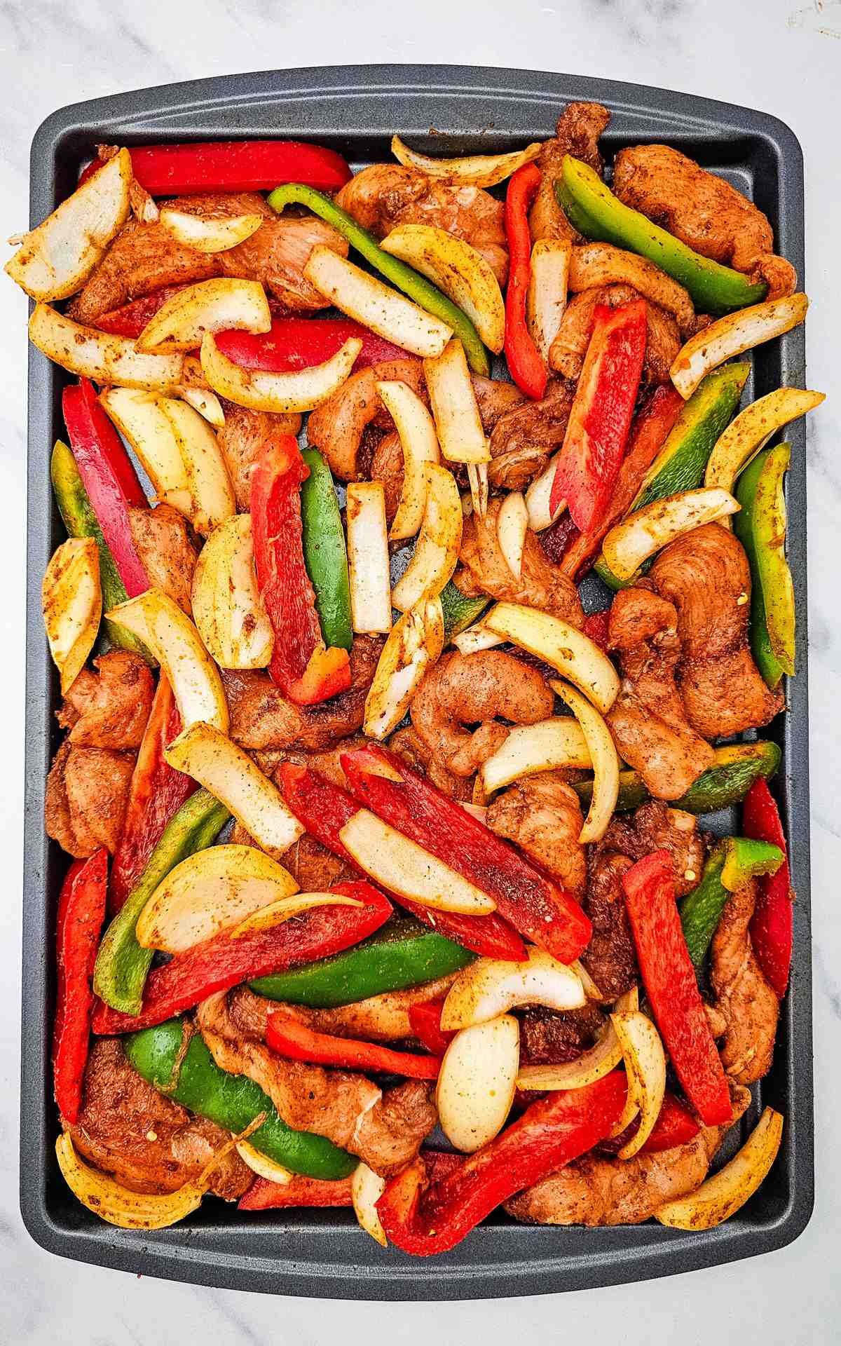 Chicken fajita ingredients on a sheet pan before being baked.
