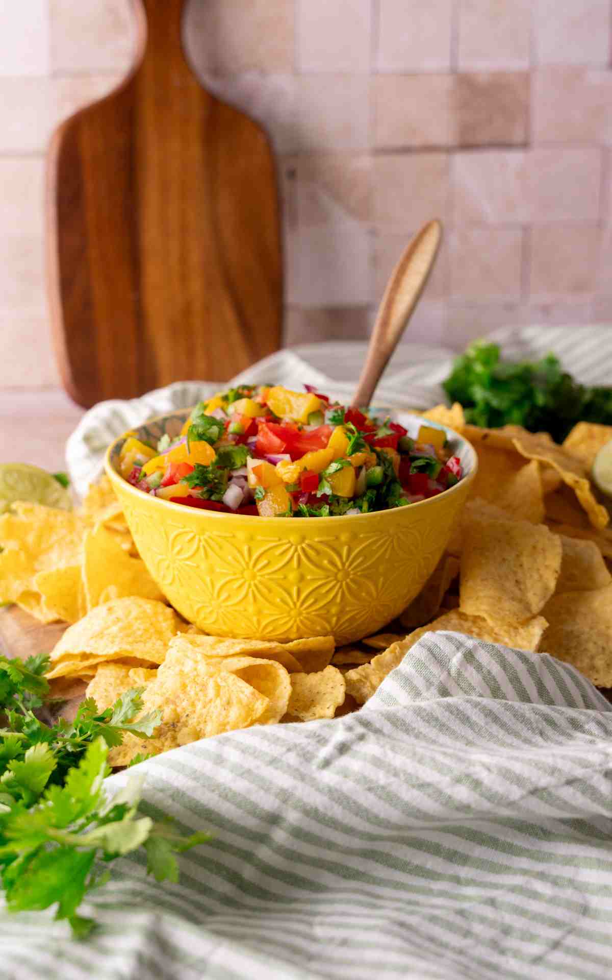Tortilla chips around a small bowl of fruit salsa made with peaches and fresh vegetables.