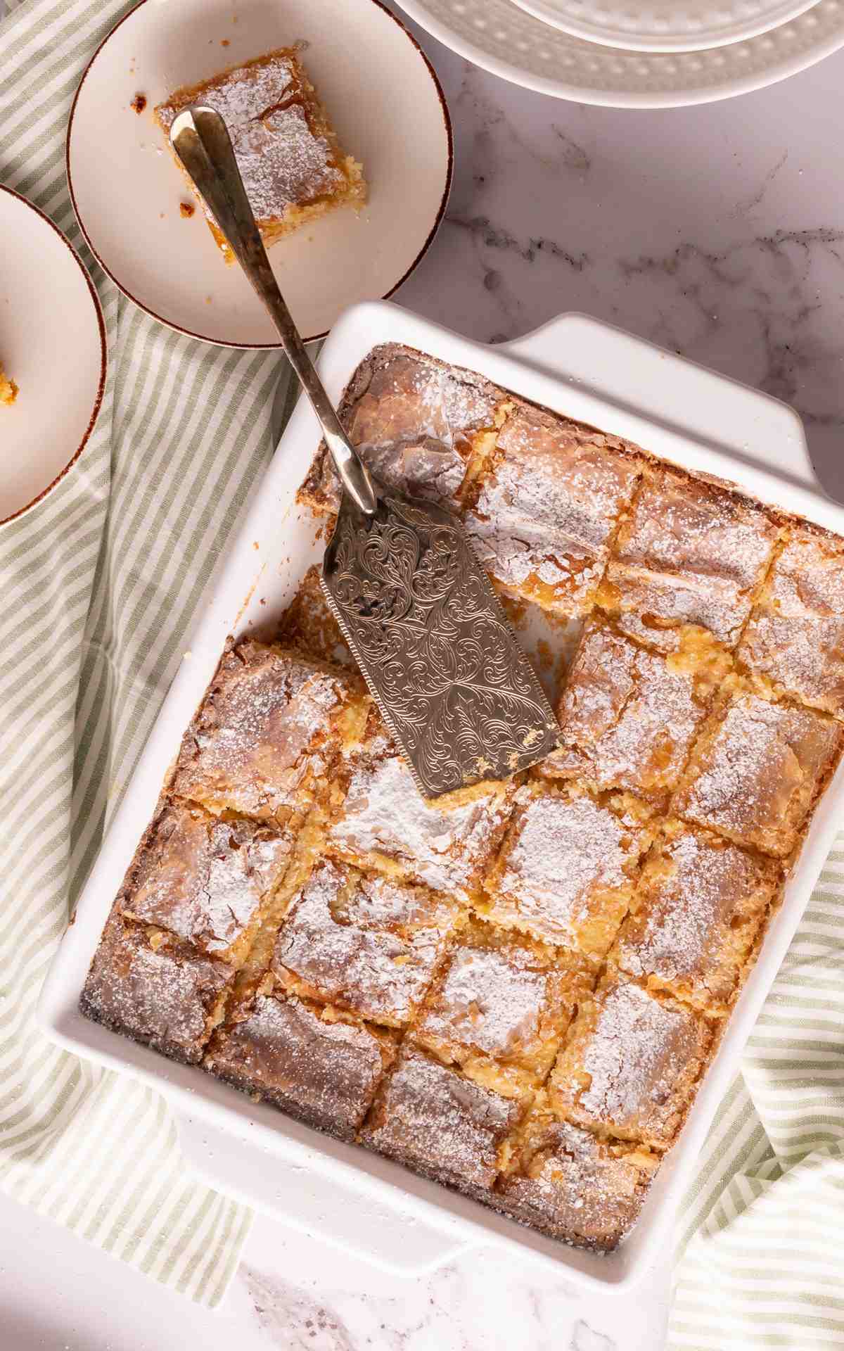A baking dish with cut slices of ooey gooey butter cake dusted with powdered sugar.