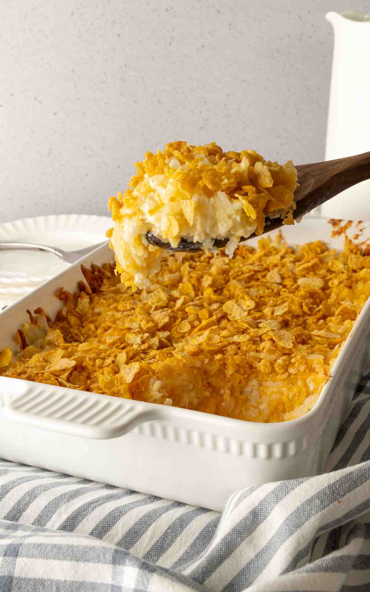 A serving spoon with a scoop of funeral potatoes with crunchy cornflake topping.